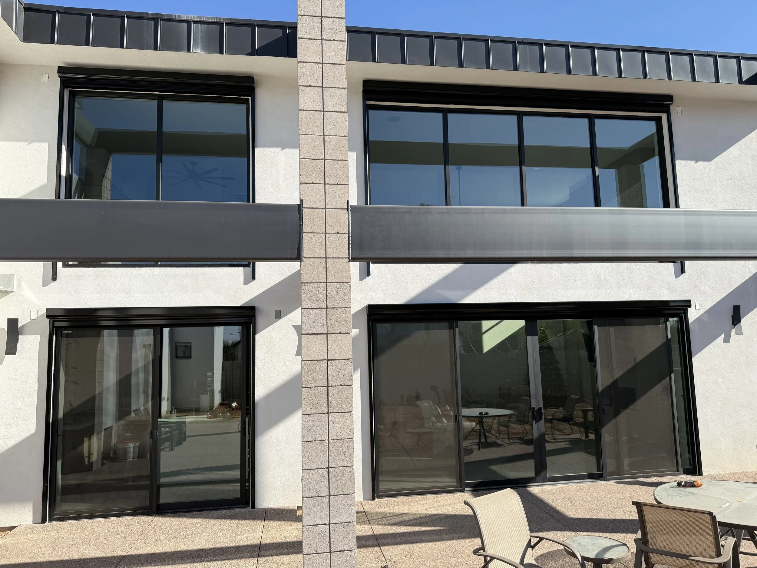 Modern two-story building with large glass sliding doors, windows, and a patio area with outdoor chairs and a table.
