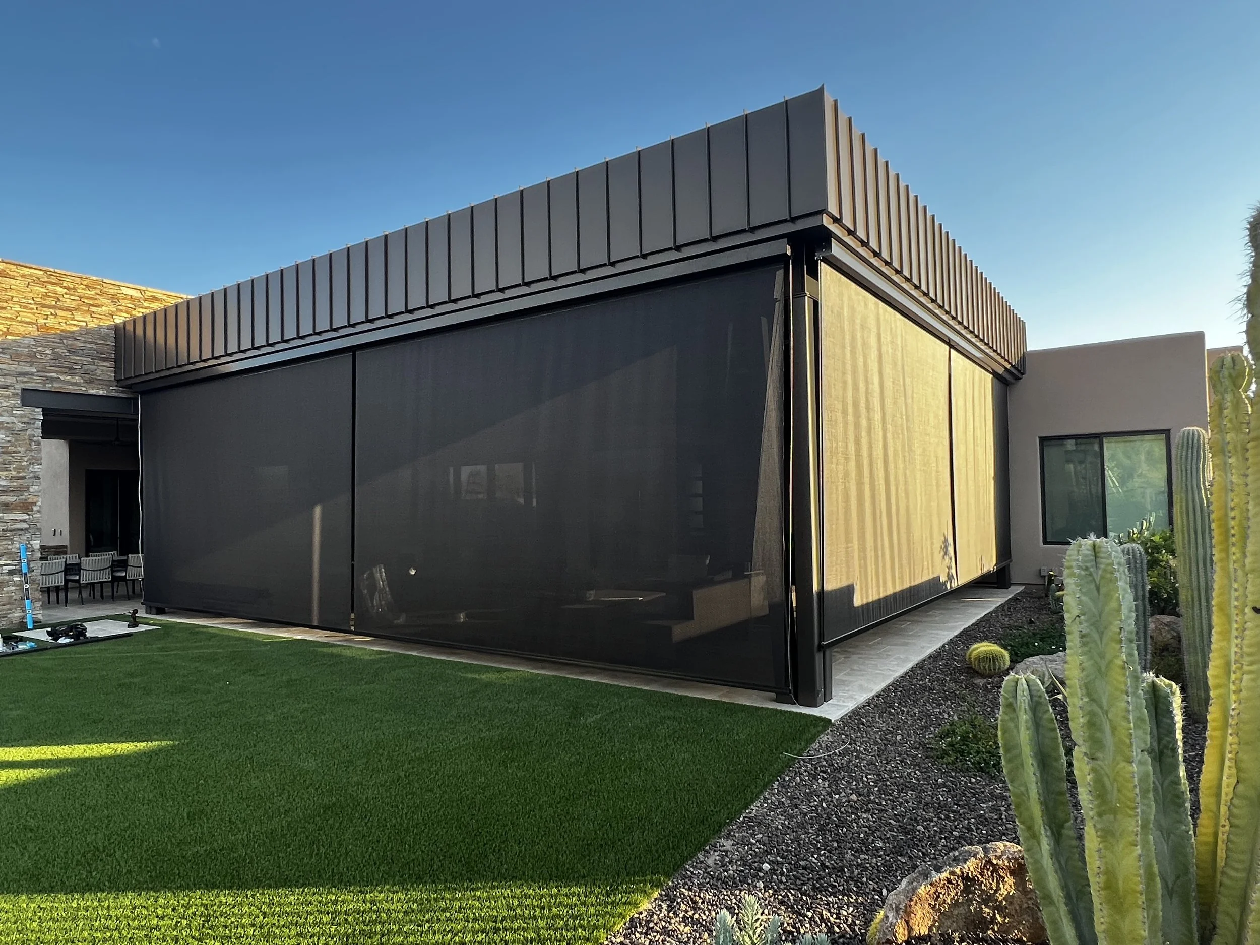 Modern house with dark exterior, large windows, and desert landscaping with cacti