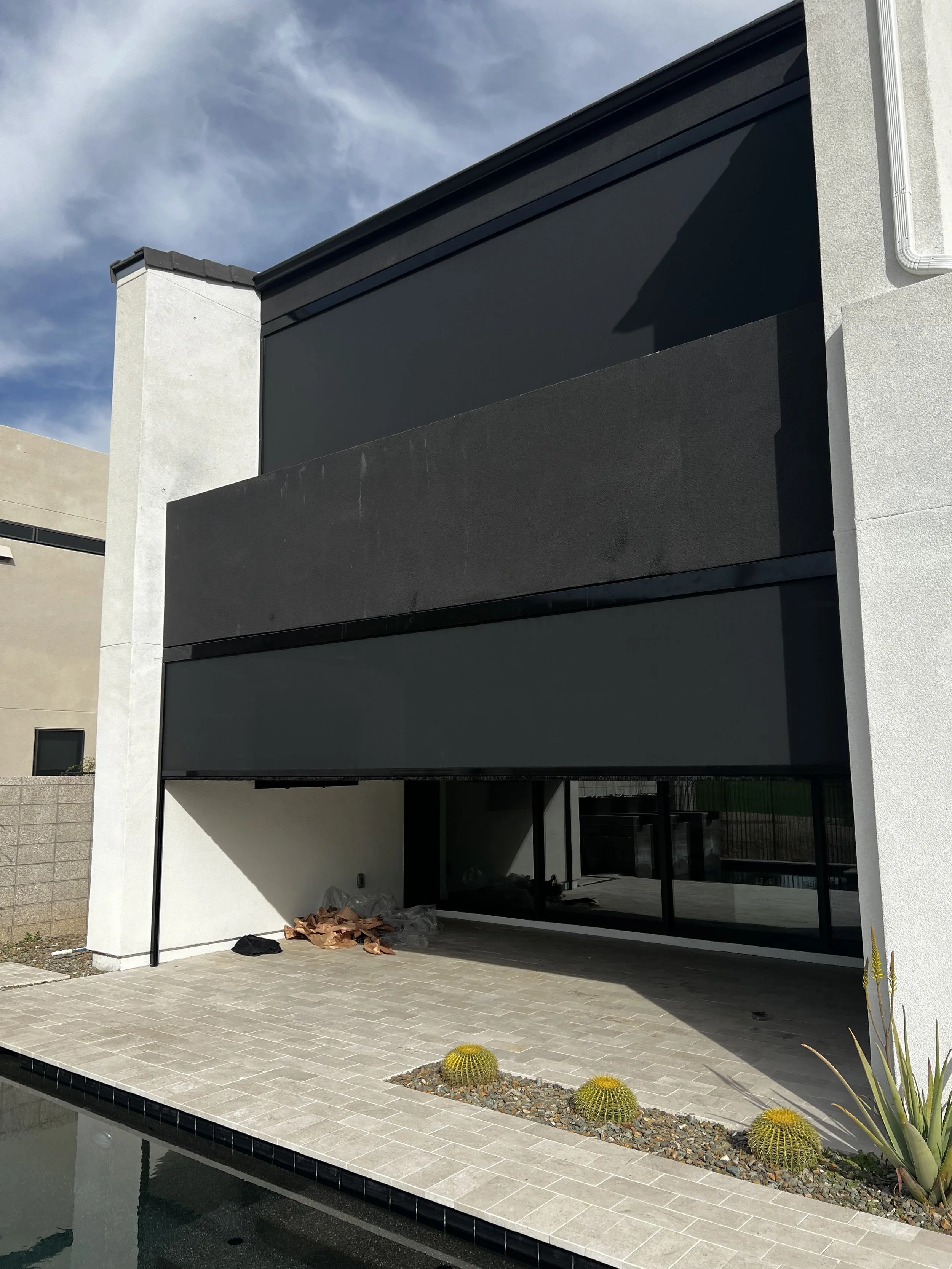 Modern residential building with black and white exterior, large glass sliding door, a patio with a small pool, and desert plants including three round cacti.