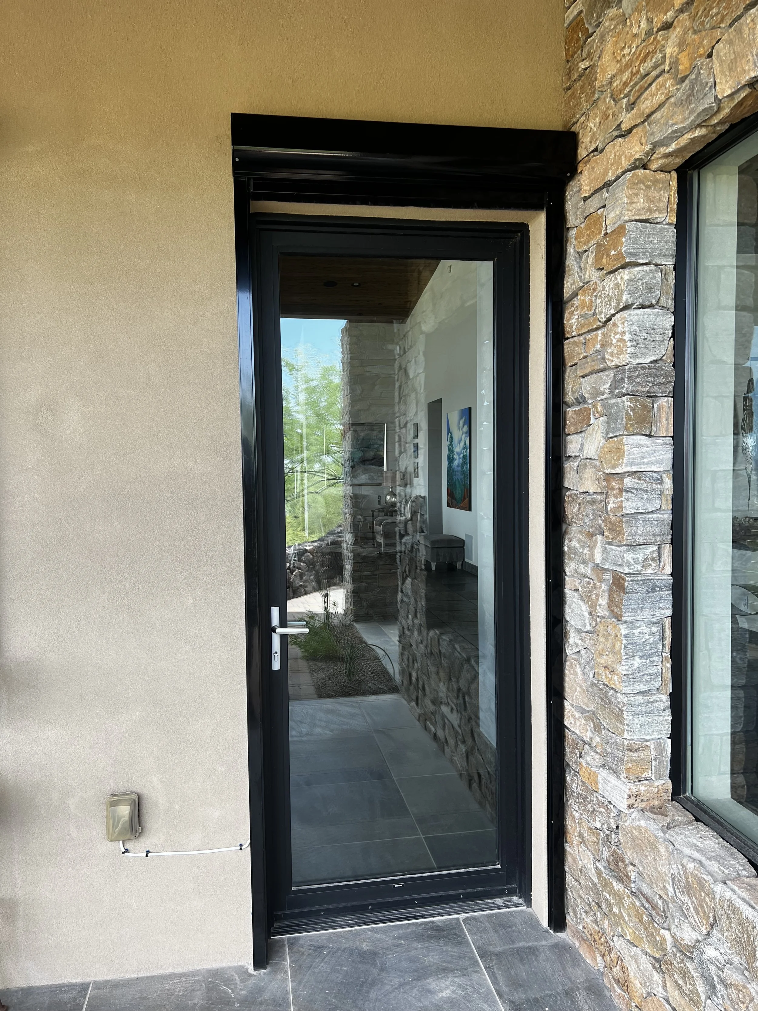 Glass exterior door with black frame next to a stone wall, view into a modern interior with artwork on the wall.