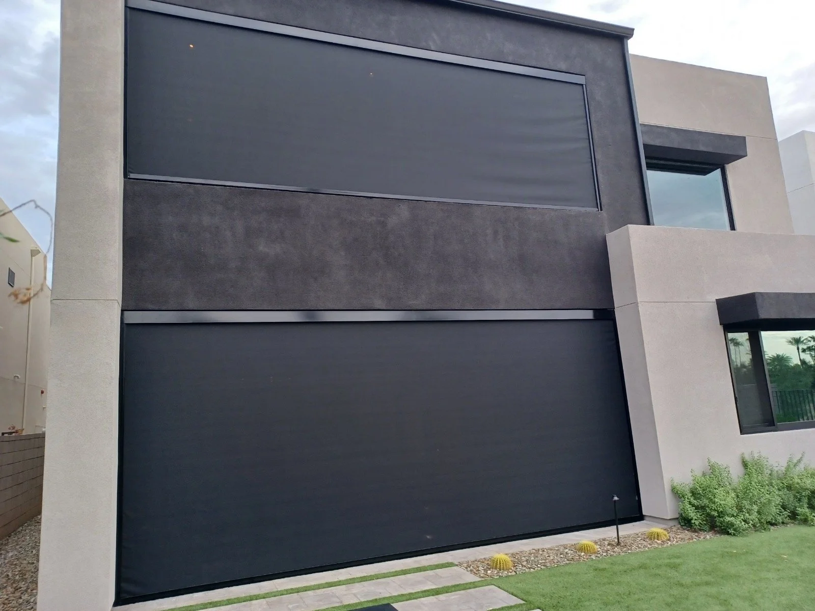 Modern multi-story house with black garage doors, large windows, and minimal landscaping.