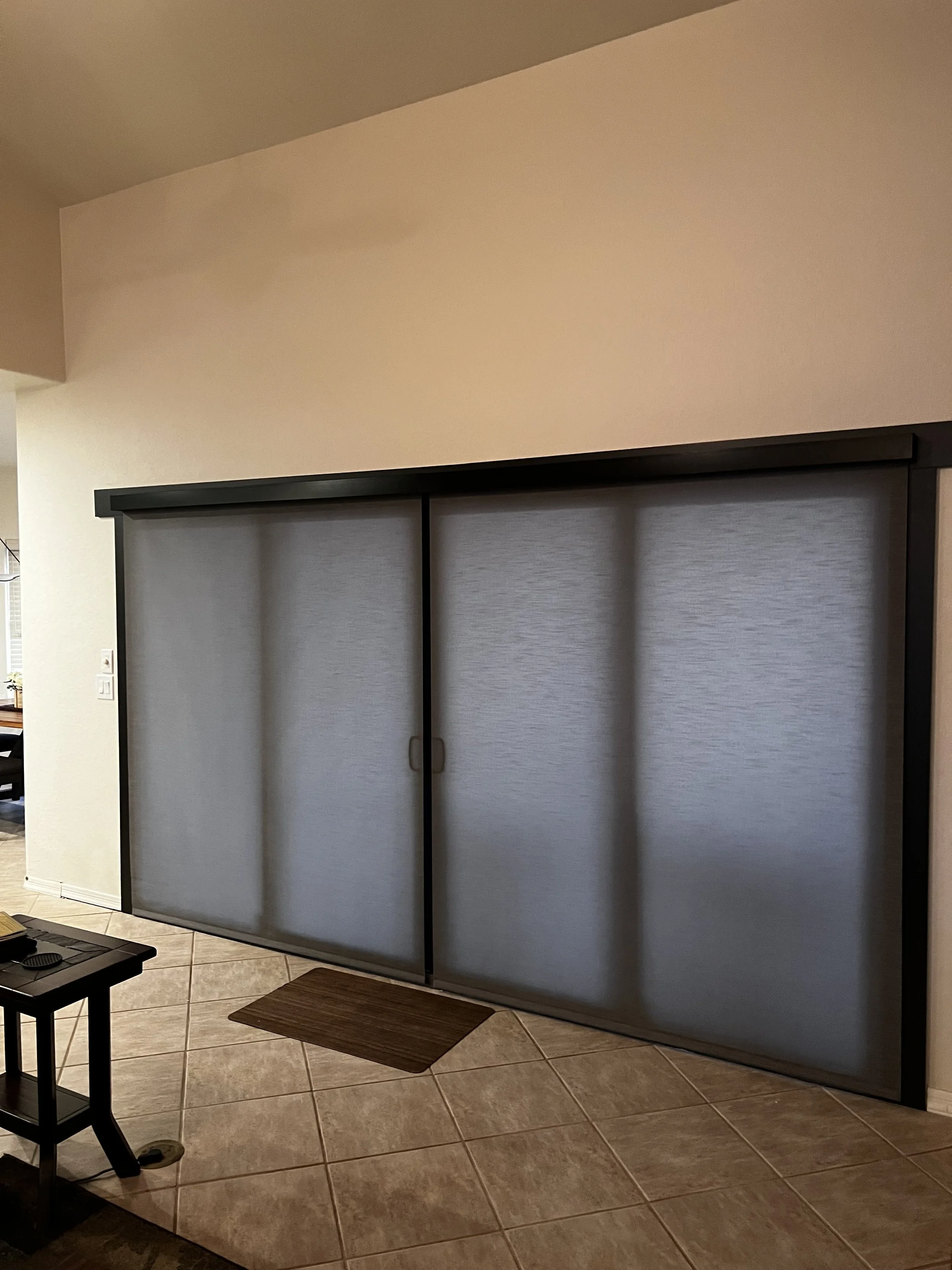 Sliding closet with grey textured doors in a hallway with tiled flooring and a small brown doormat in front.