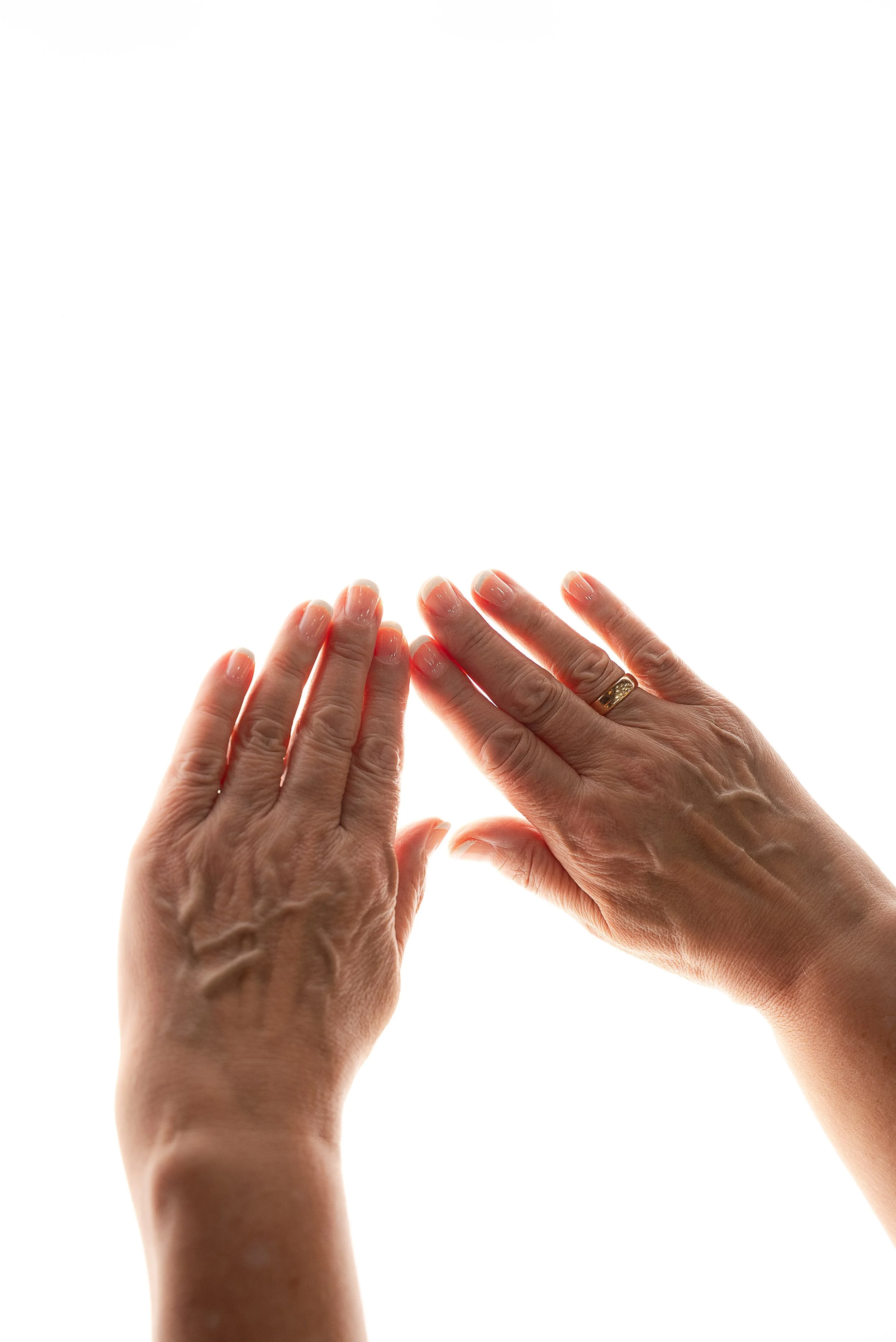Close-up of two hands: one with a wedding ring, the other with painted nails, touching against a white background.