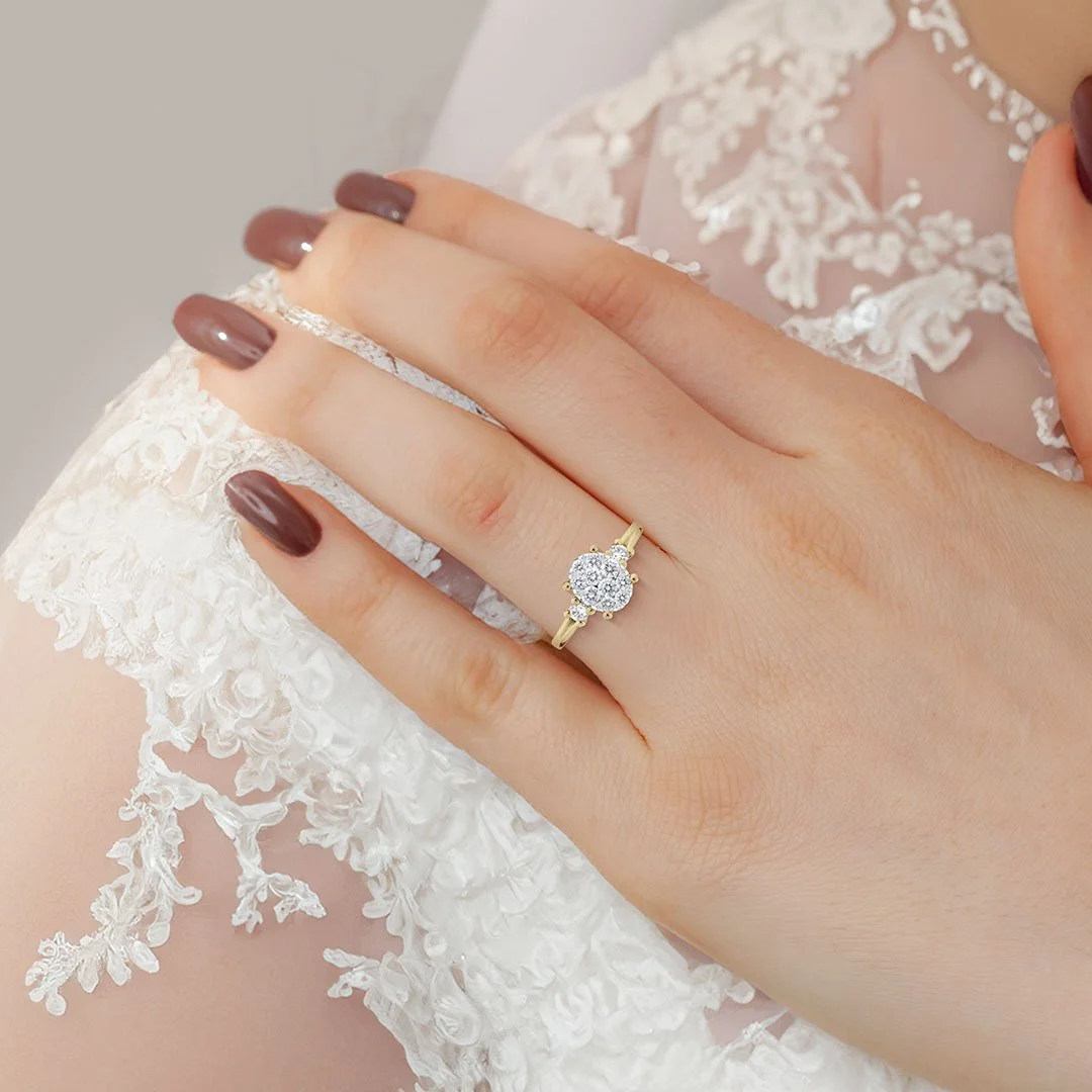A woman wearing a diamond engagement ring with a round center stone and pave diamonds on a yellow gold band.