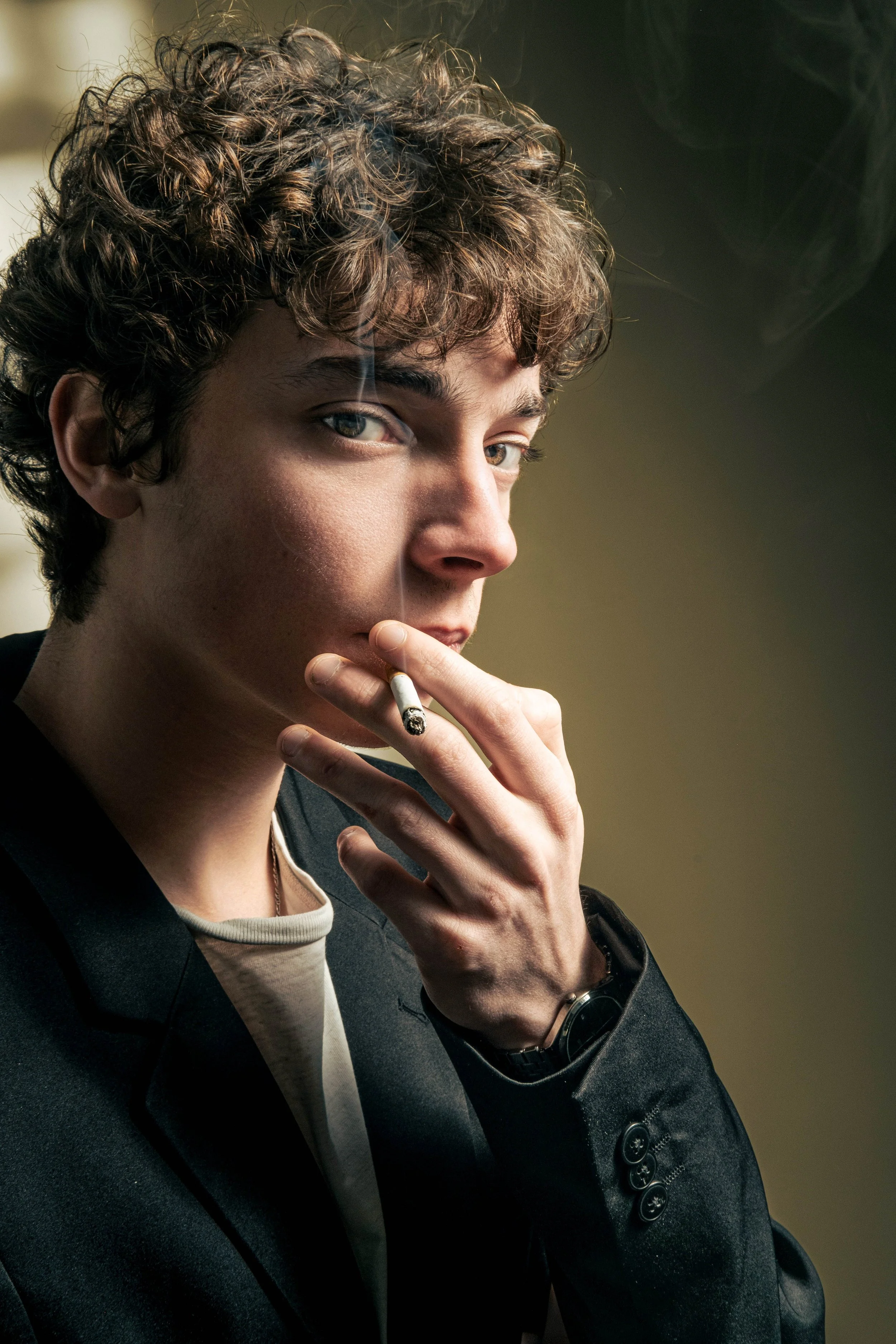 Un homme en costume fume une cigarette. Il regarde l'objectif.