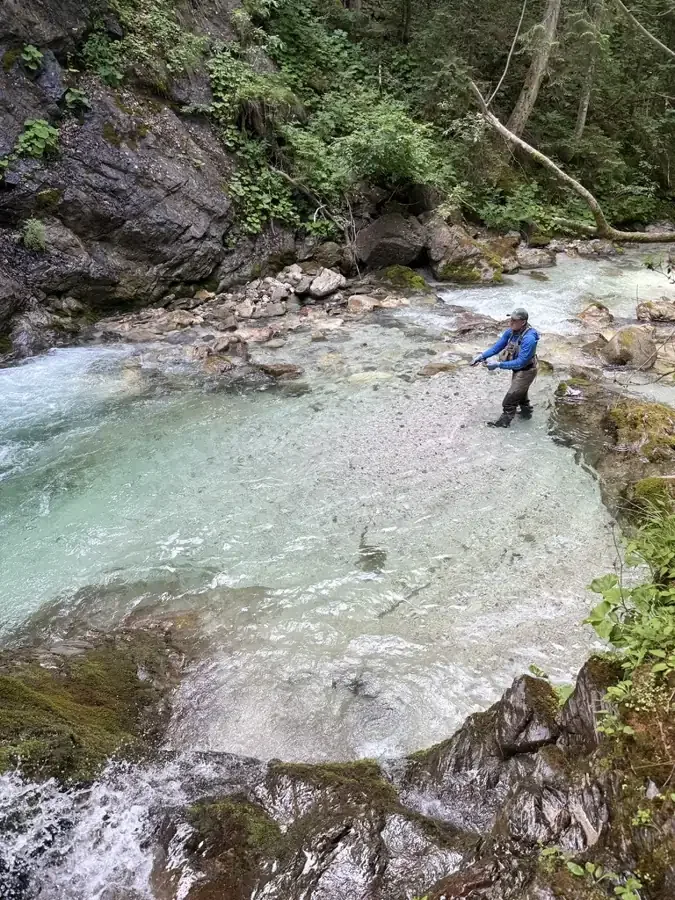 Fly fisherman fishing an alpine river in Northern Italy, surrounded by rocks and forest.