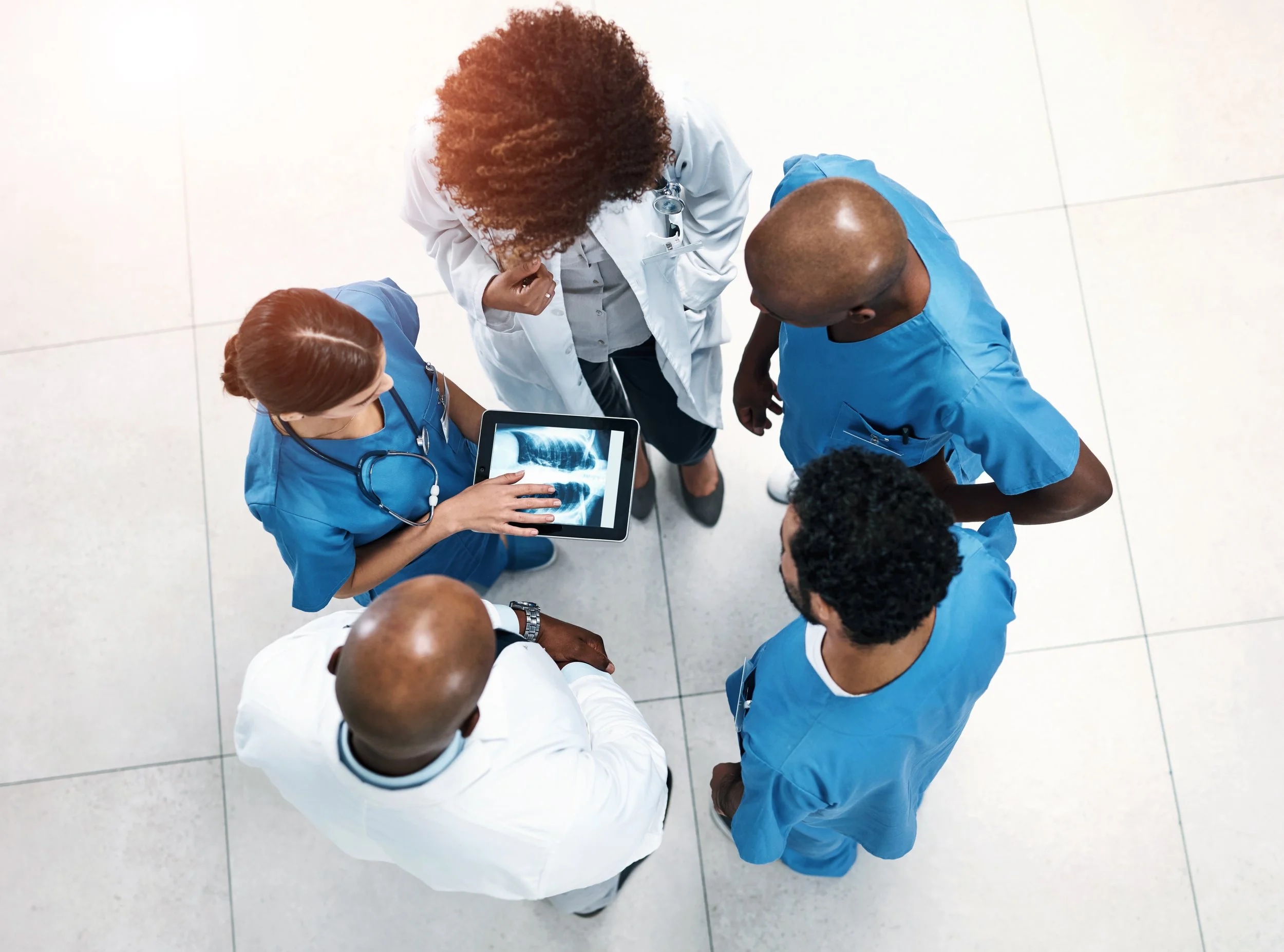Five healthcare providers discuss a treatment plan with the image of a patient X-ray on an iPd between them