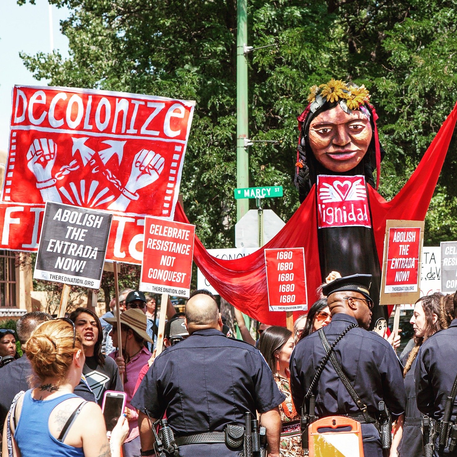 Dignidad - Indigenous ancestor puppet hovers over police at a disruption of colonial fiesta celebration in O'ga P'ogeh NM.