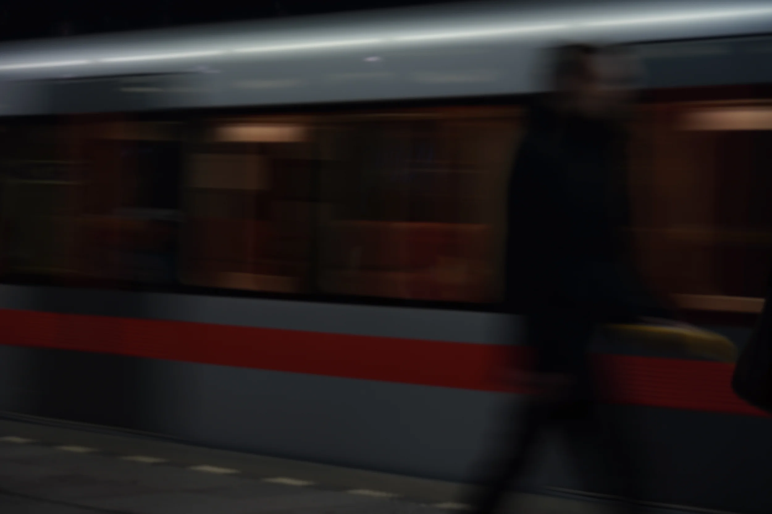 Moving train with a person walking nearby in a dimly lit setting.