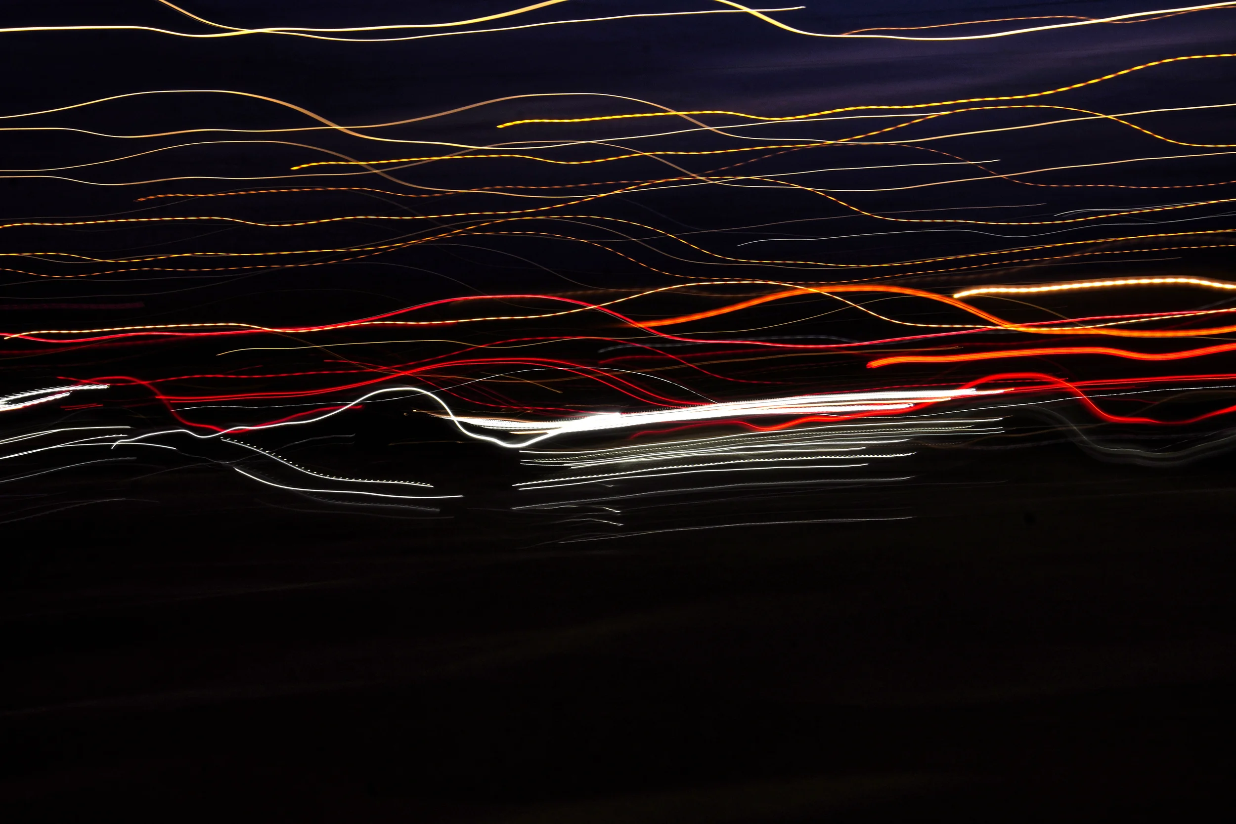 Abstract light trails at night with streaks of yellow, white, and red lights against a dark background.