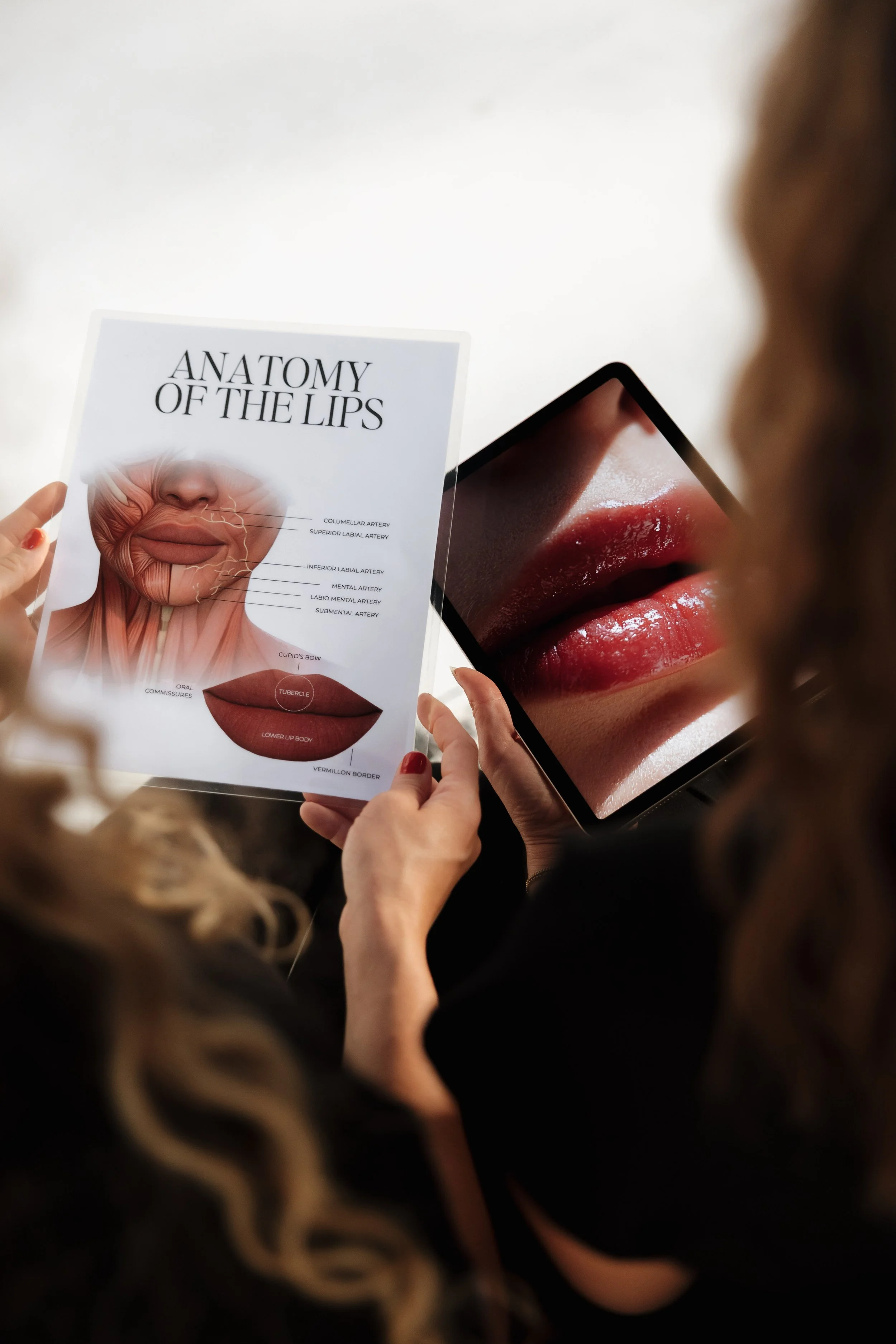 Person holding a booklet titled 'Anatomy of the Lips' and a tablet showing a close-up image of lips.