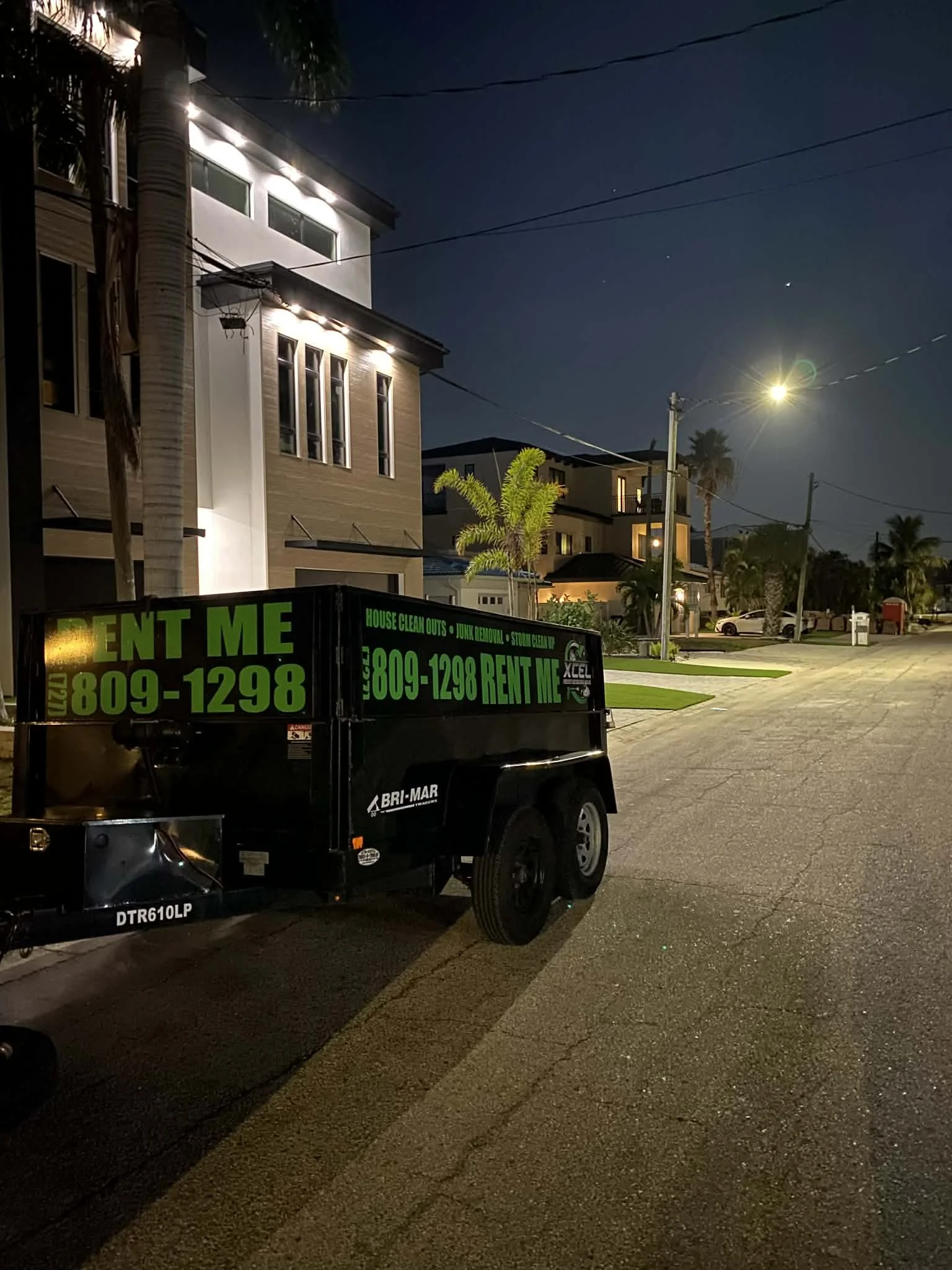 A backyard scene with a dirt and grassy path, a wooden fence, a covered object or vehicle, a tree, a parked white truck, and a gray trailer. The top of the image shows the time and date as Tuesday at 7:28 AM.
