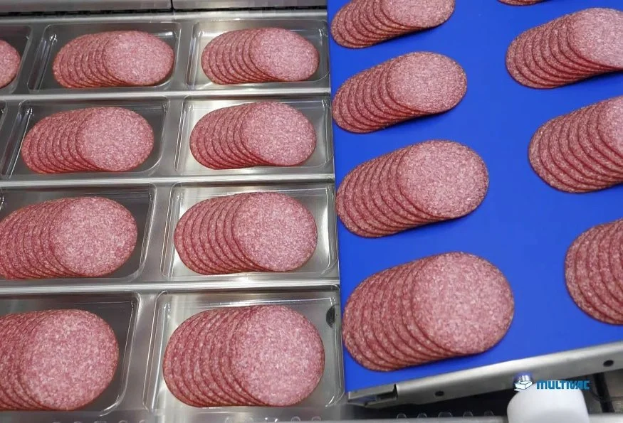 Slices of salami arranged in stacks, on a metal surface and blue cutting board.
