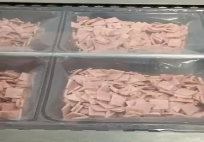Several trays filled with sliced process ham slices in a display case.