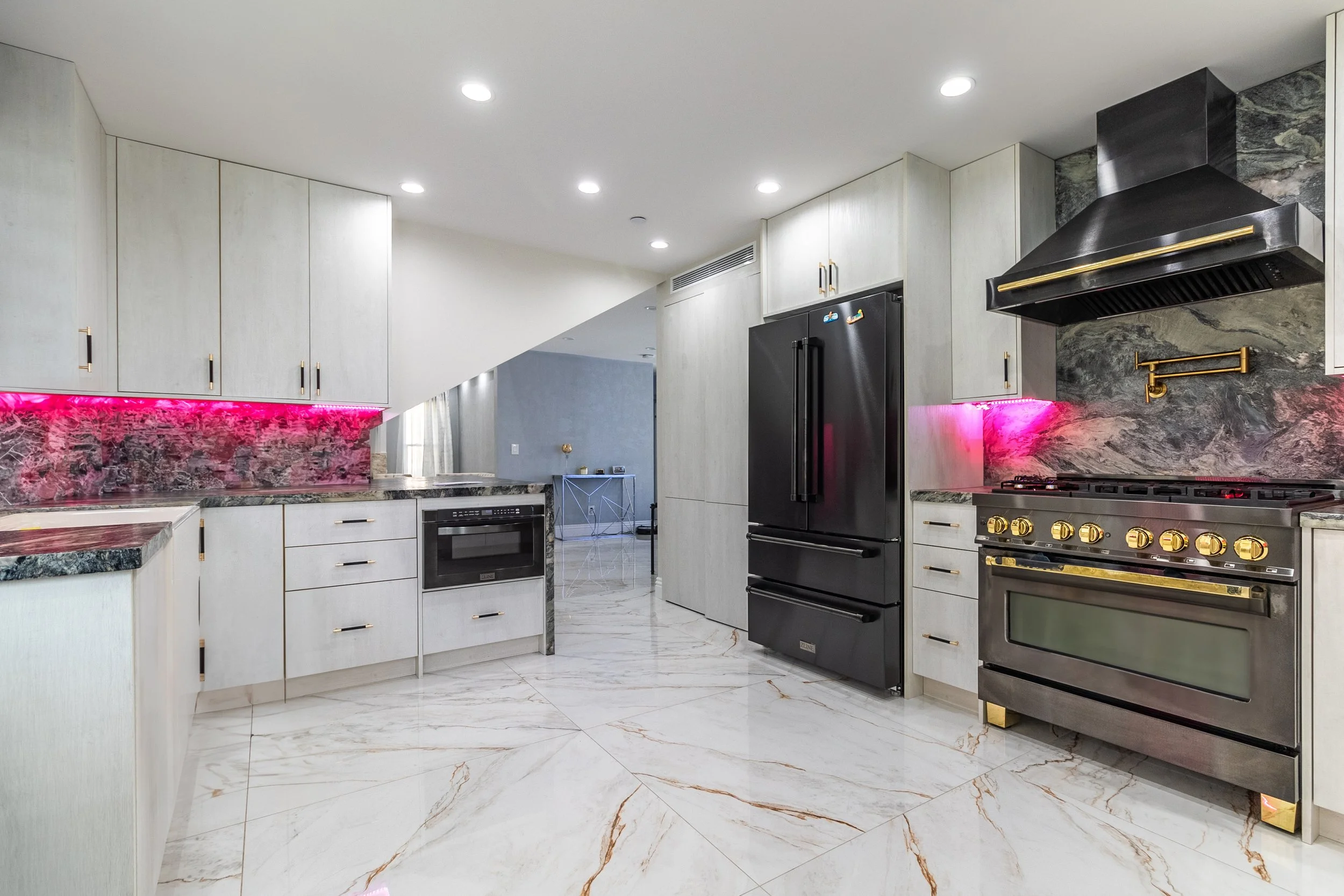 Modern kitchen with white cabinetry, black appliances, pink LED lighting under the cabinets, marble countertops, and a marble backsplash. Features include a stove, oven, refrigerator, and a range hood.