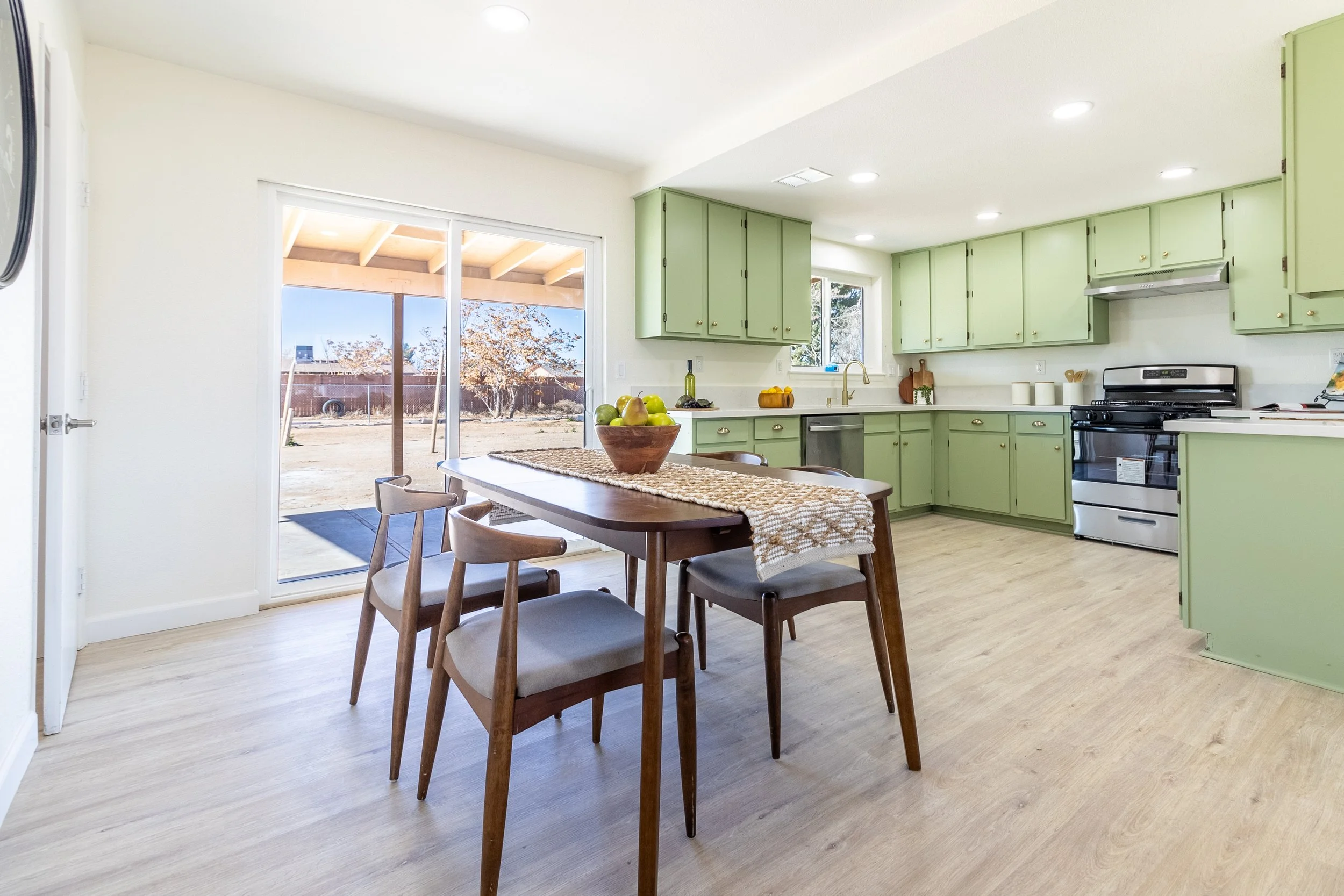 Kitchen with light green cabinets, black stove, dining table with four chairs, and sliding glass doors leading to backyard.