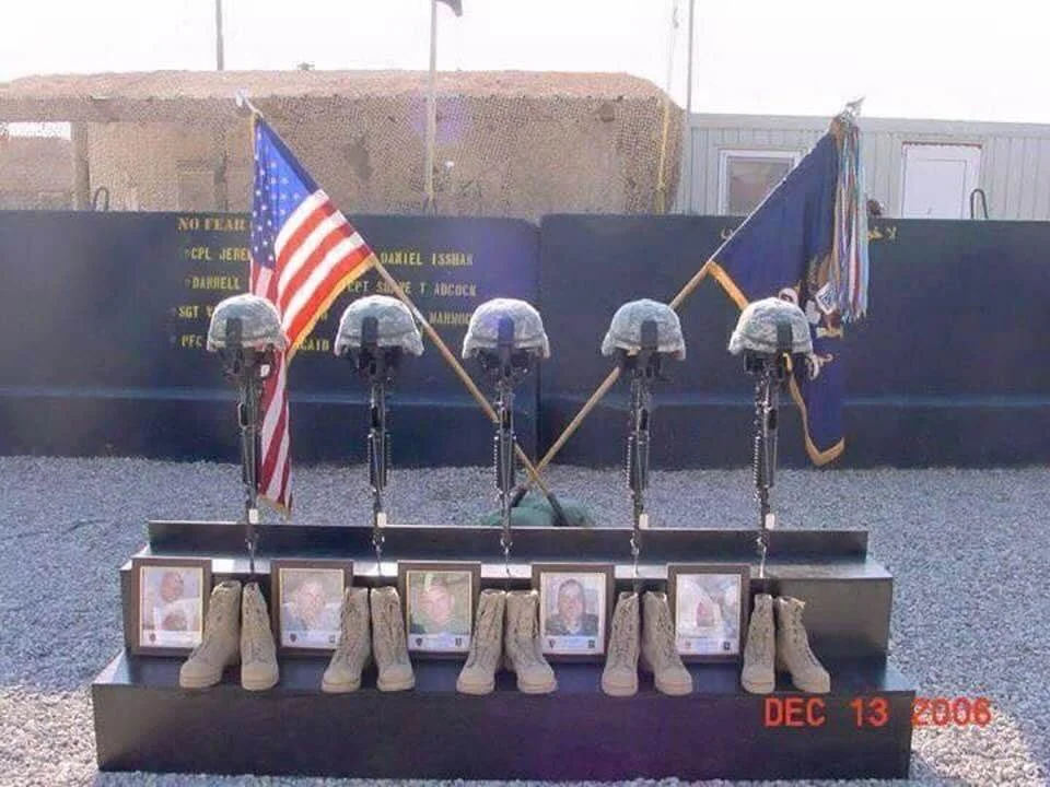 Memorial display featuring military helmets, boots, and framed photos of soldiers, with American flags in the background, commemorating fallen soldiers on December 13, 2006.