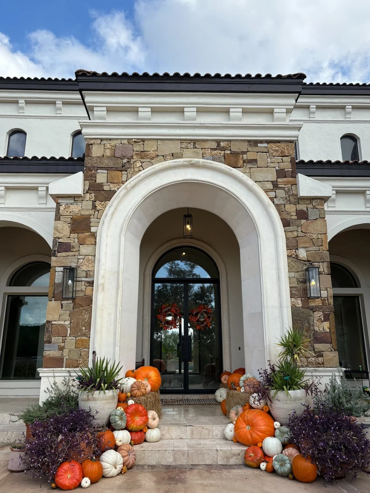 Grand stone archway entrance of a Mediterranean-style estate home in Boerne, Texas decorated with a fall pumpkin display, Package #1 by The Pumpkin Parlor