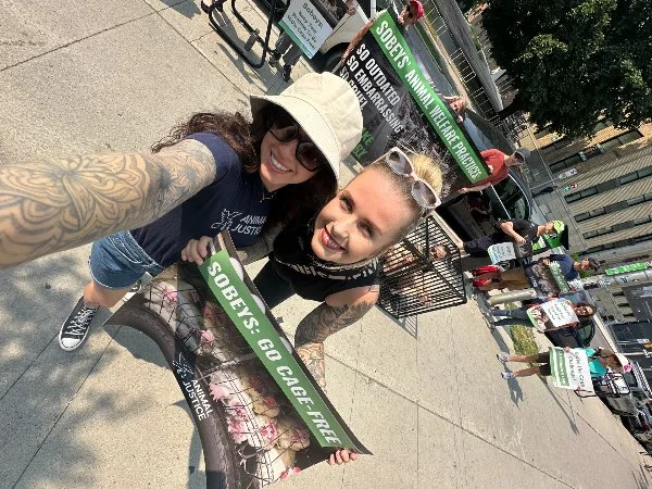 Two women protesting outdoors, holding signs advocating for cannabis legalization and police reform, with other protesters in the background.