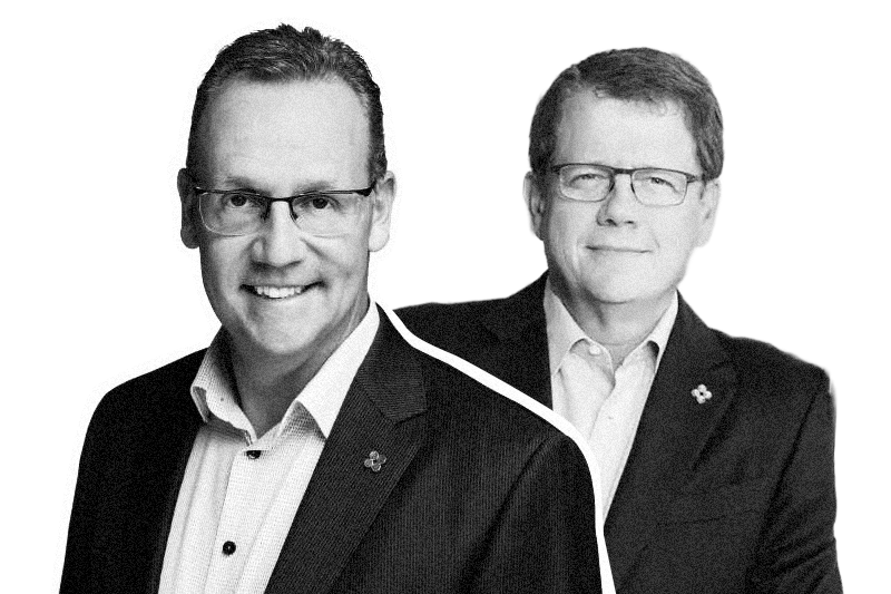 Two men in suits and glasses, smiling, in a black and white photo with a white outline around their silhouettes.