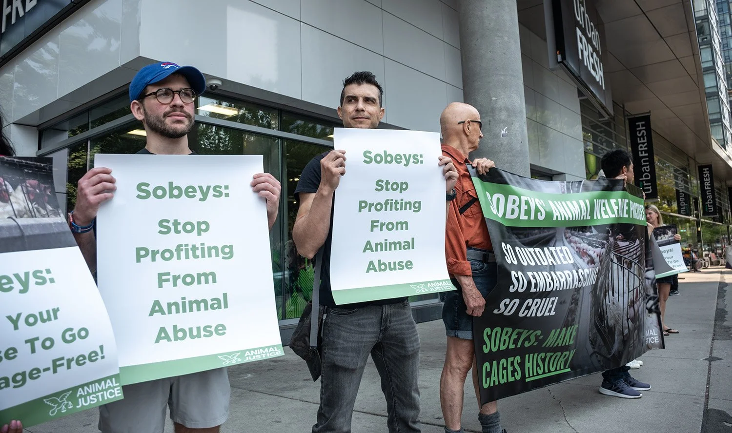 People protesting outside a building holding signs and banners opposing animal cruelty and animal abuse, advocating for animal rights and justice.
