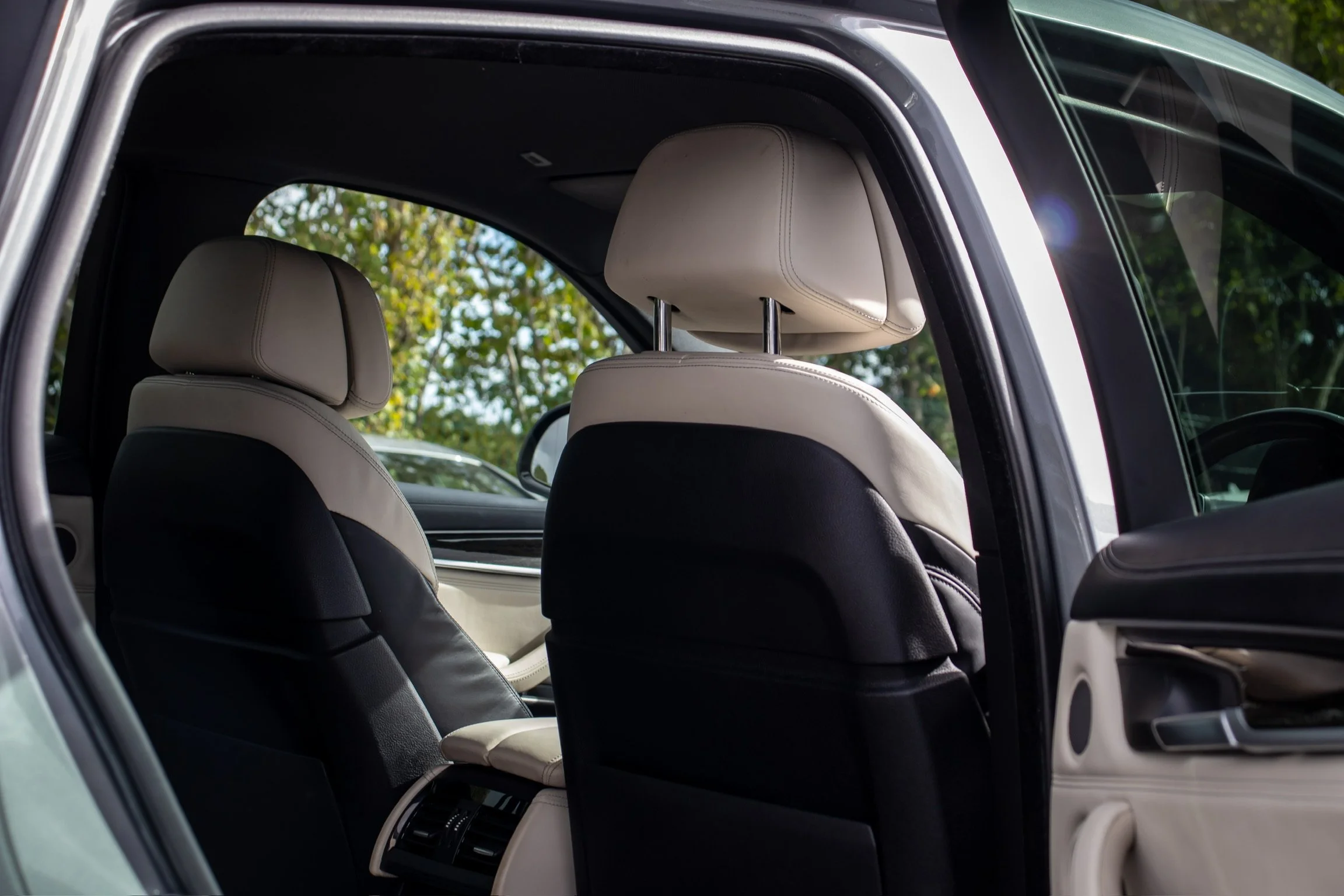 Interior view of a car showing front seats with beige and black upholstery and a back seat area with a view of trees outside the window.