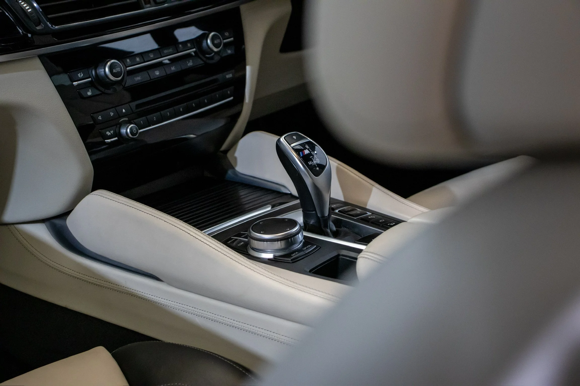 Interior of a luxury car showing a gear shift lever, control dial, and climate control panel with beige leather seats and black dashboard