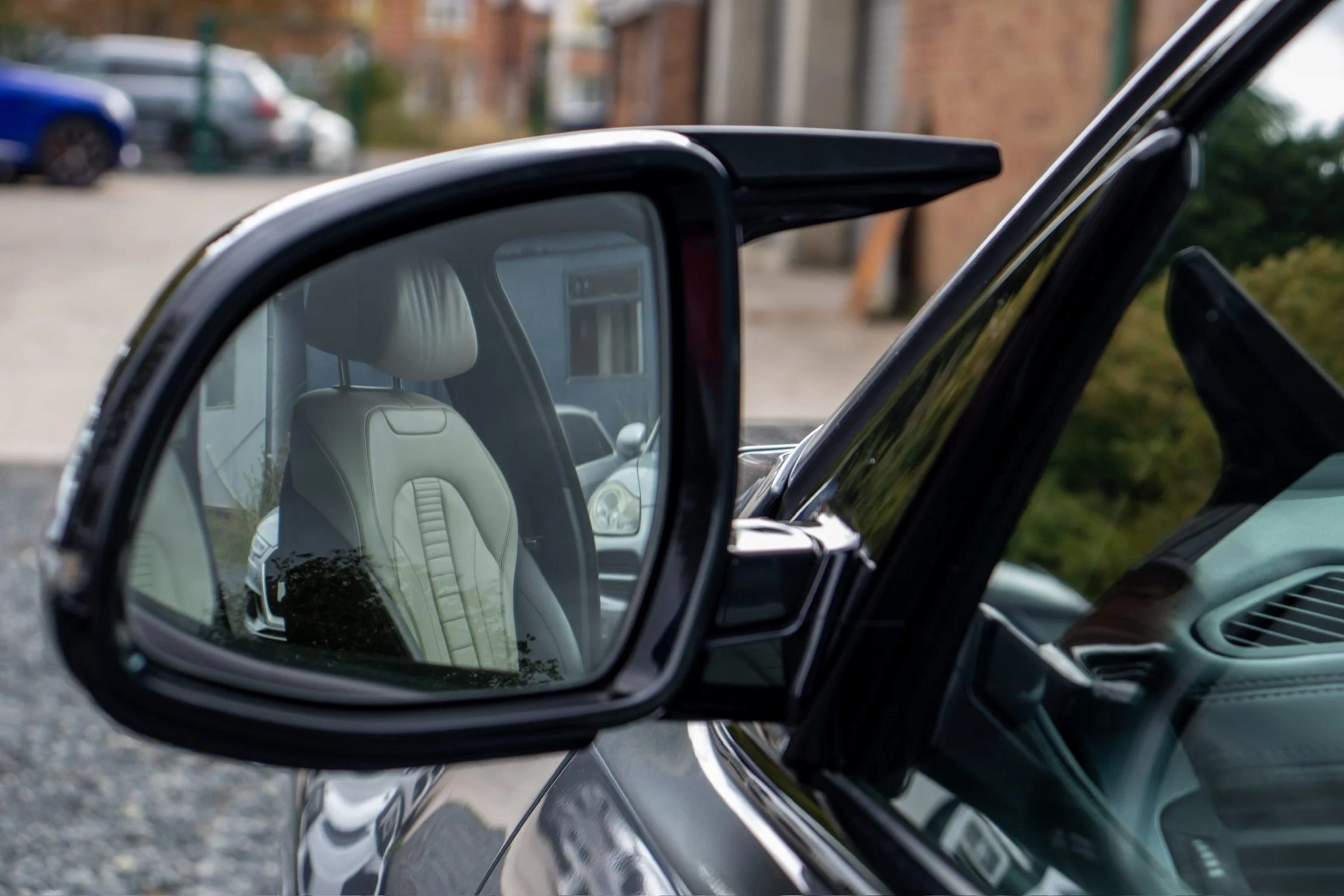 Close-up of a car's side mirror reflecting a beige leather seat with an adjustable headrest inside the vehicle.