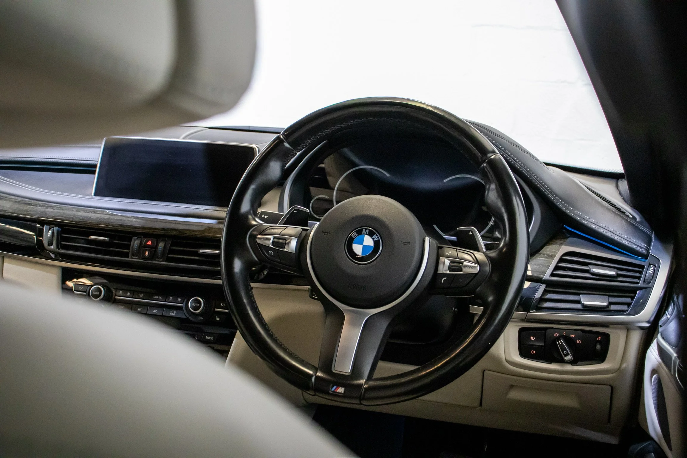Interior of a BMW car dashboard showing the steering wheel with BMW logo, digital instrument cluster, central display screen, air vents, and climate control buttons.