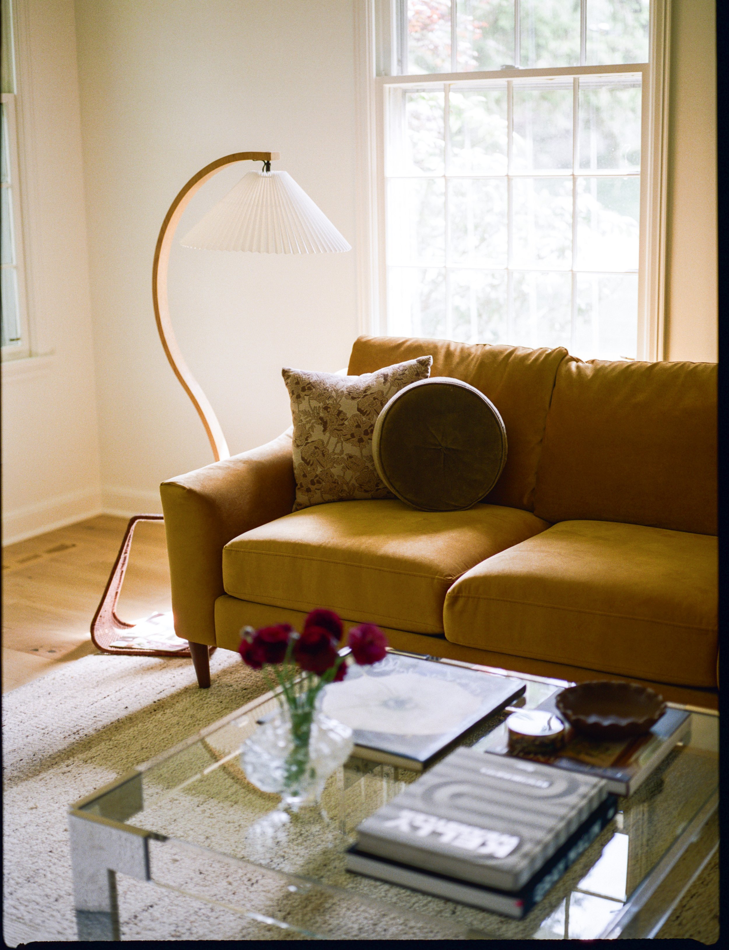 Modern living room scene with mustard velvet sofa, sculptural floor lamp, and glass coffee table. Interior photography by Natalie Folchi, focused on texture, design, and lived-in warmth.