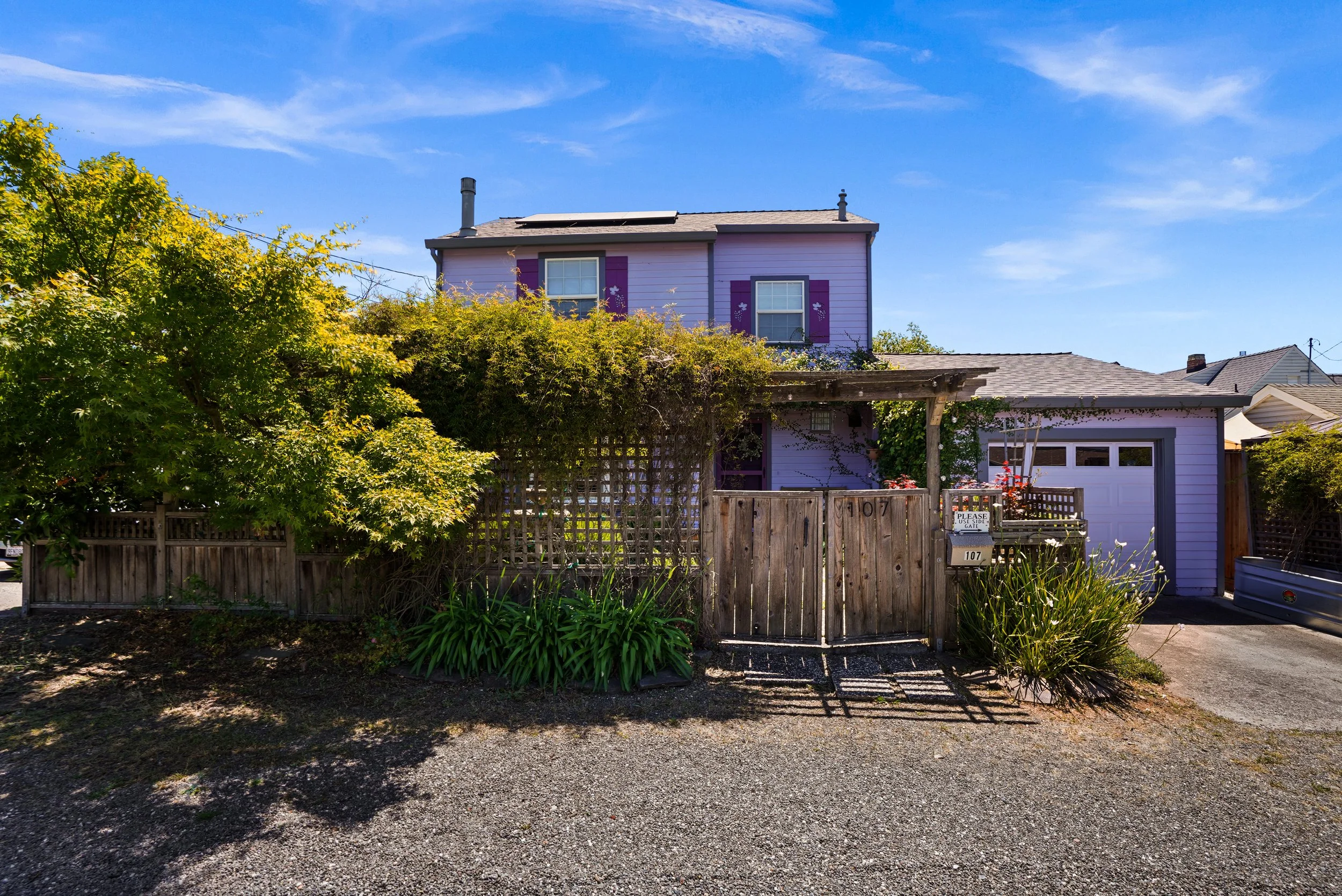 A purple house with garage doors, purple shutters, and a backyard with trees and a wooden fence.