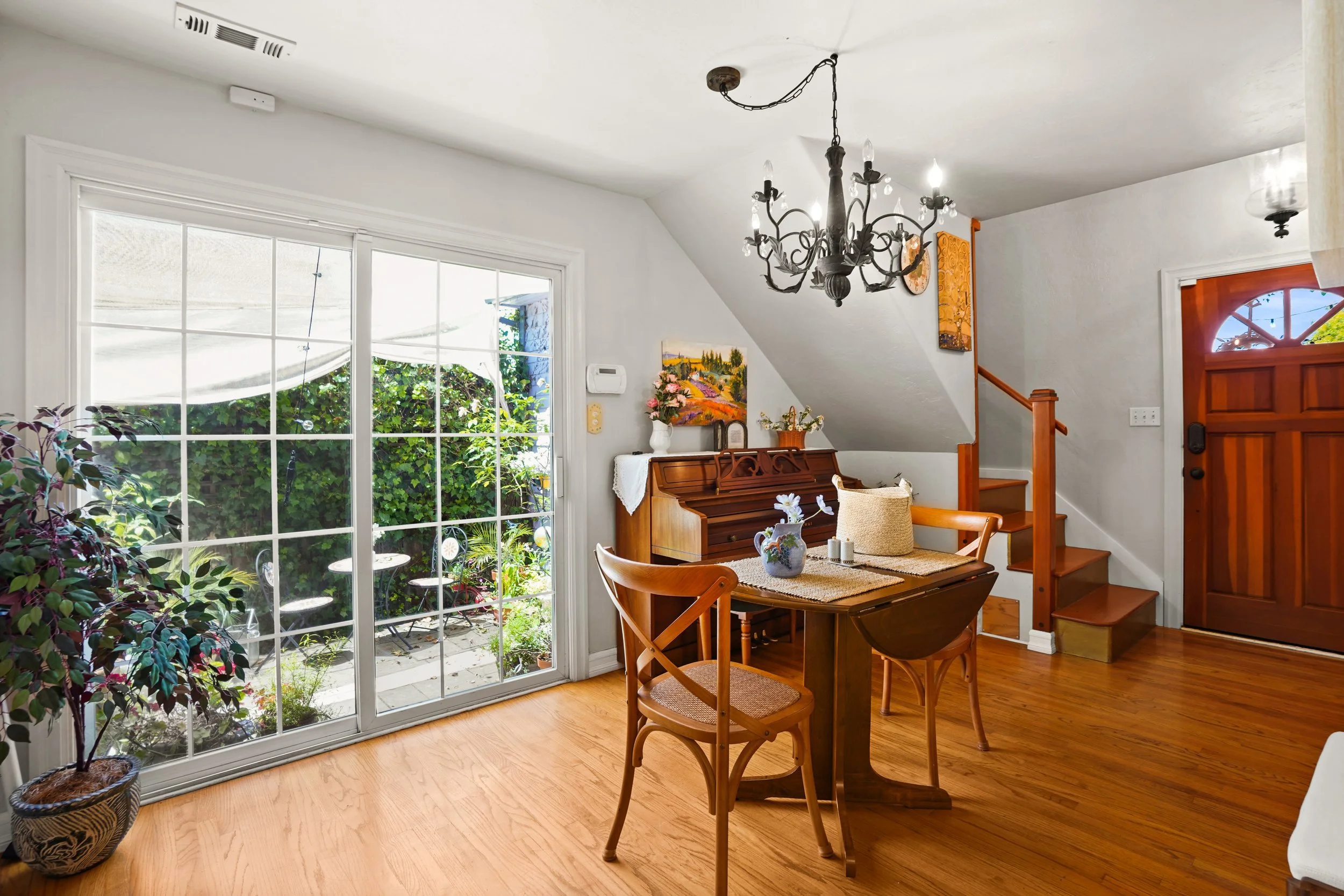 A cozy dining area with wooden furniture and a sliding glass door leading to an outdoor patio, decorated with potted plants and wall art.