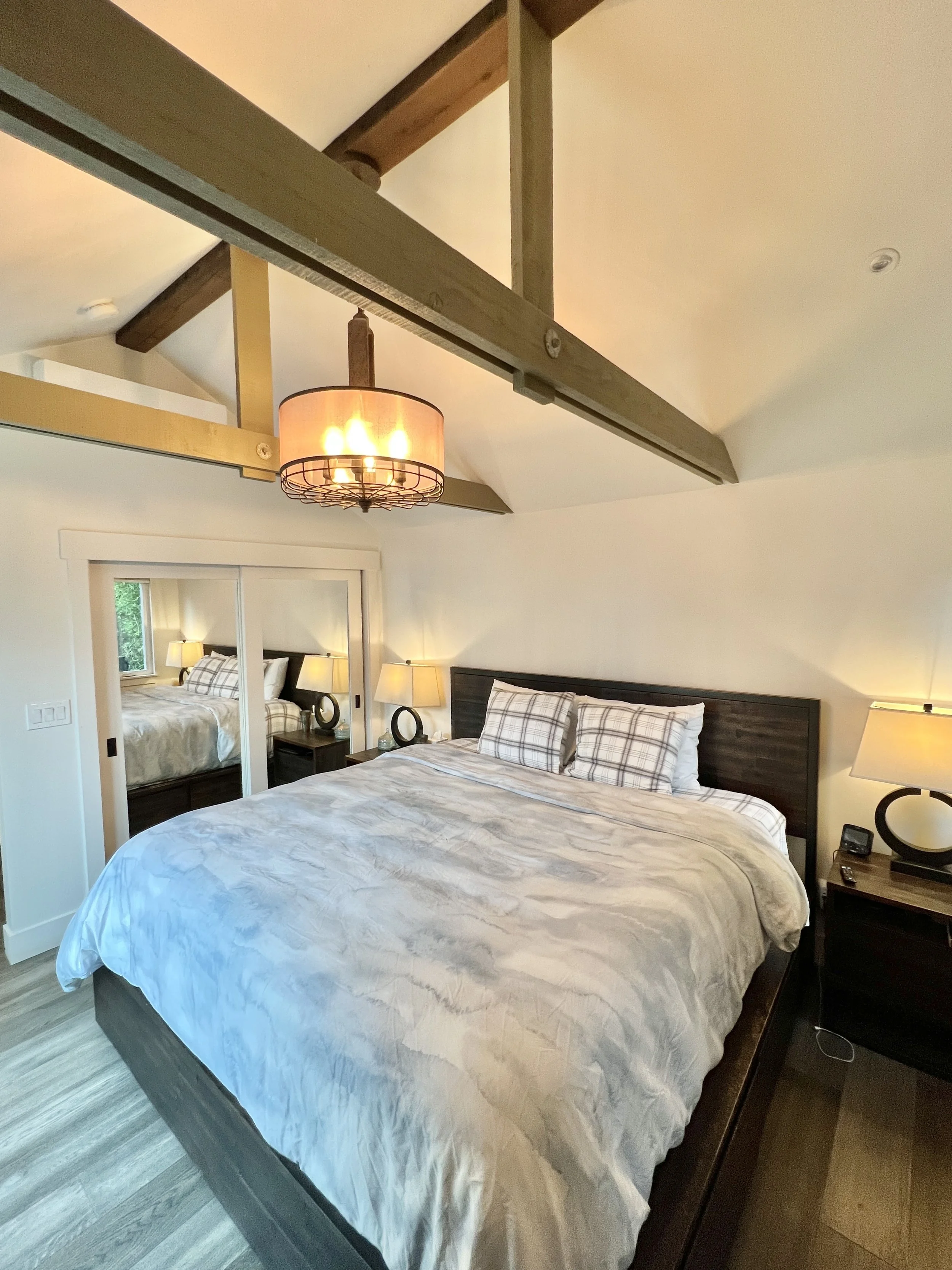 Bedroom with a large bed, plaid pillows, nightstands with lamps, and mirrored closet doors reflecting another bed.