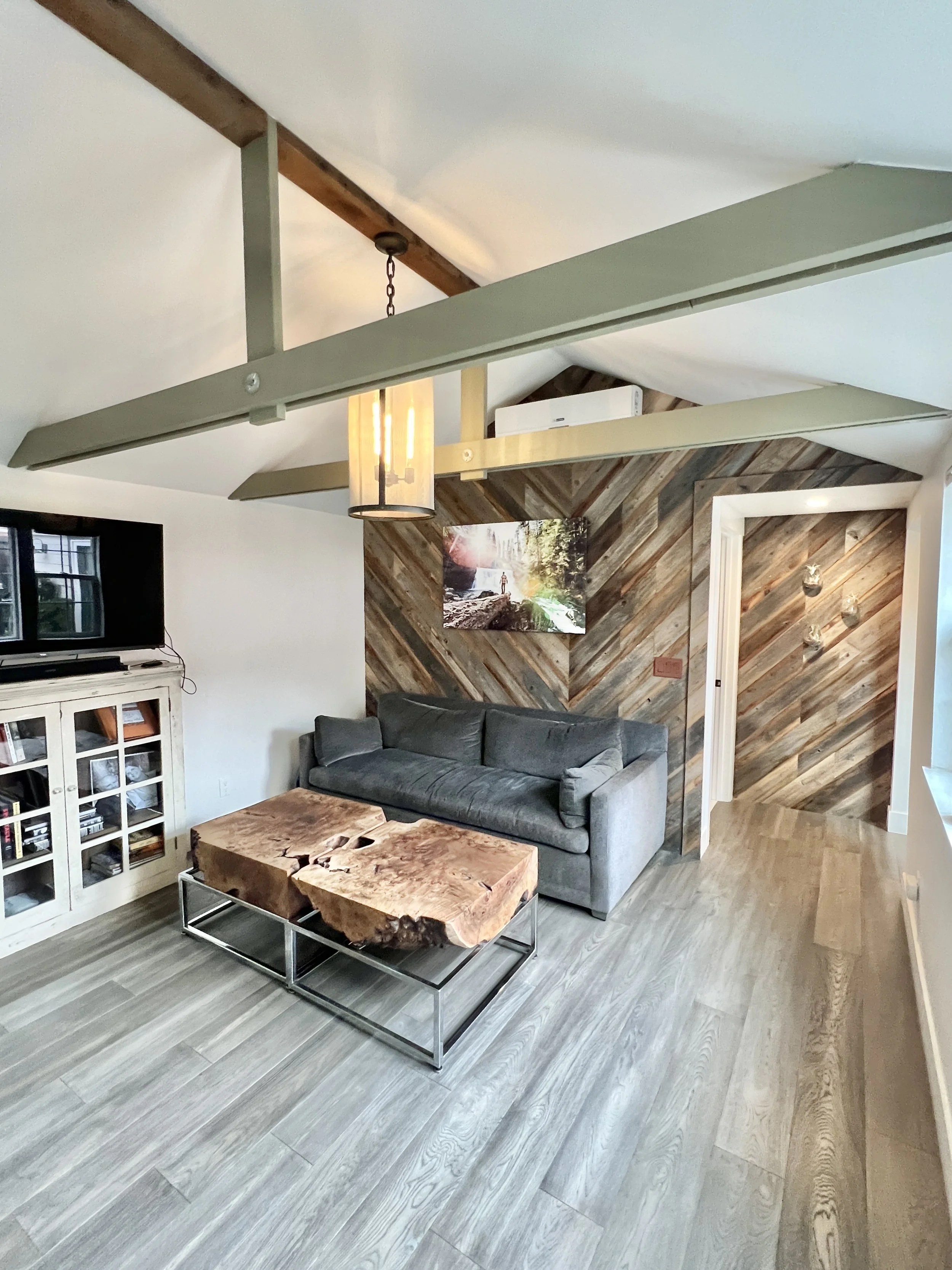 Modern living room with wood accent wall, gray sofa, live edge wooden coffee table, mounted TV, and contemporary lighting fixtures.