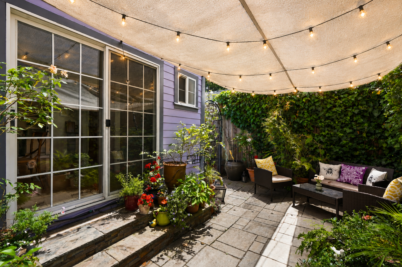 Outdoor patio with string lights, potted plants, and patio furniture against a purple house wall with sliding glass door.
