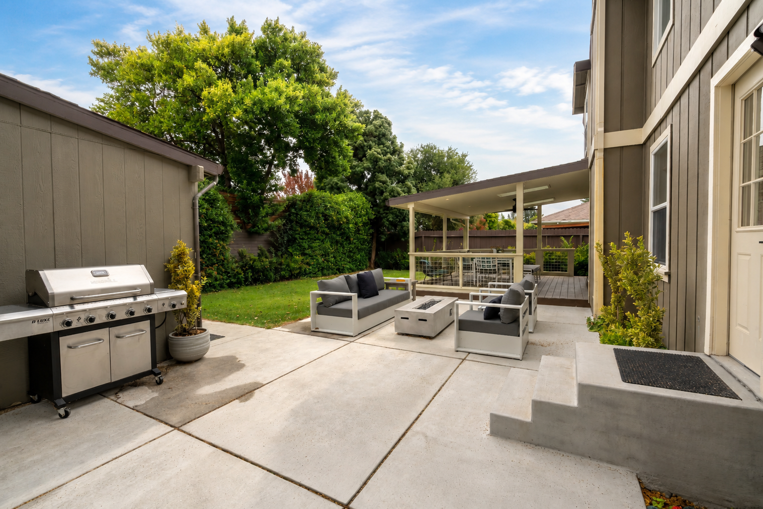Patio area with outdoor furniture, grill, and a backyard with trees and greenery.