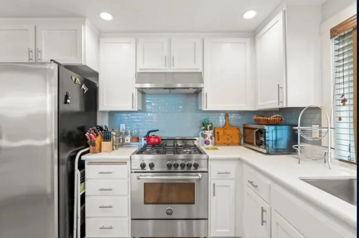 Modern white kitchen with stainless steel appliances and a blue backsplash.