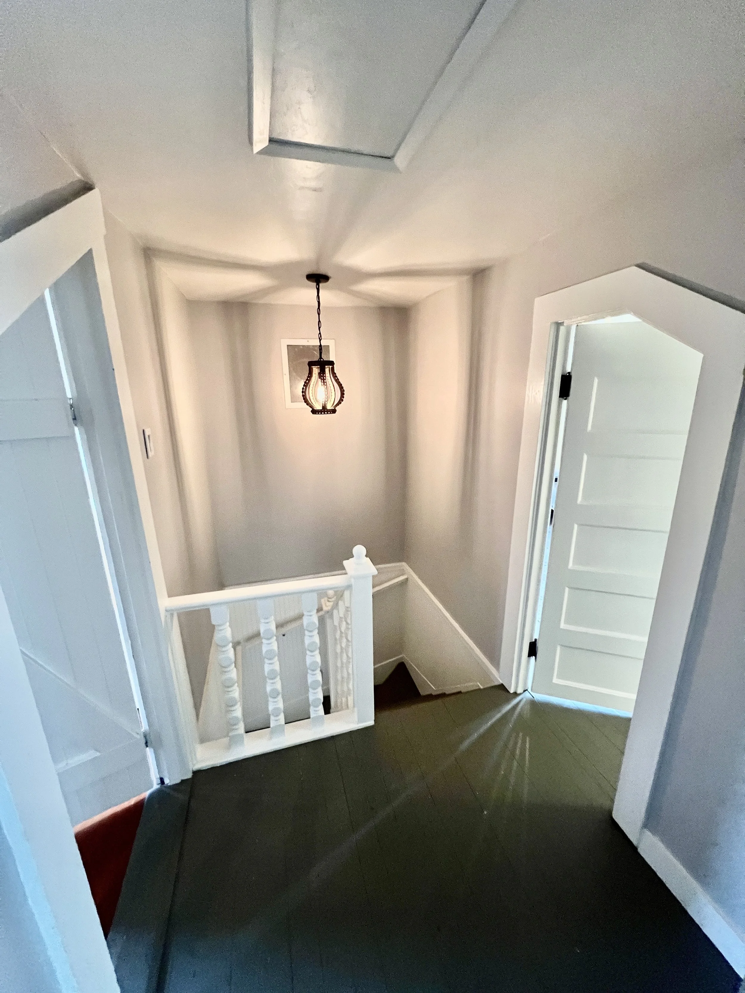 View of an upstairs hallway with a staircase, white doors, gray walls, and a hanging light fixture.