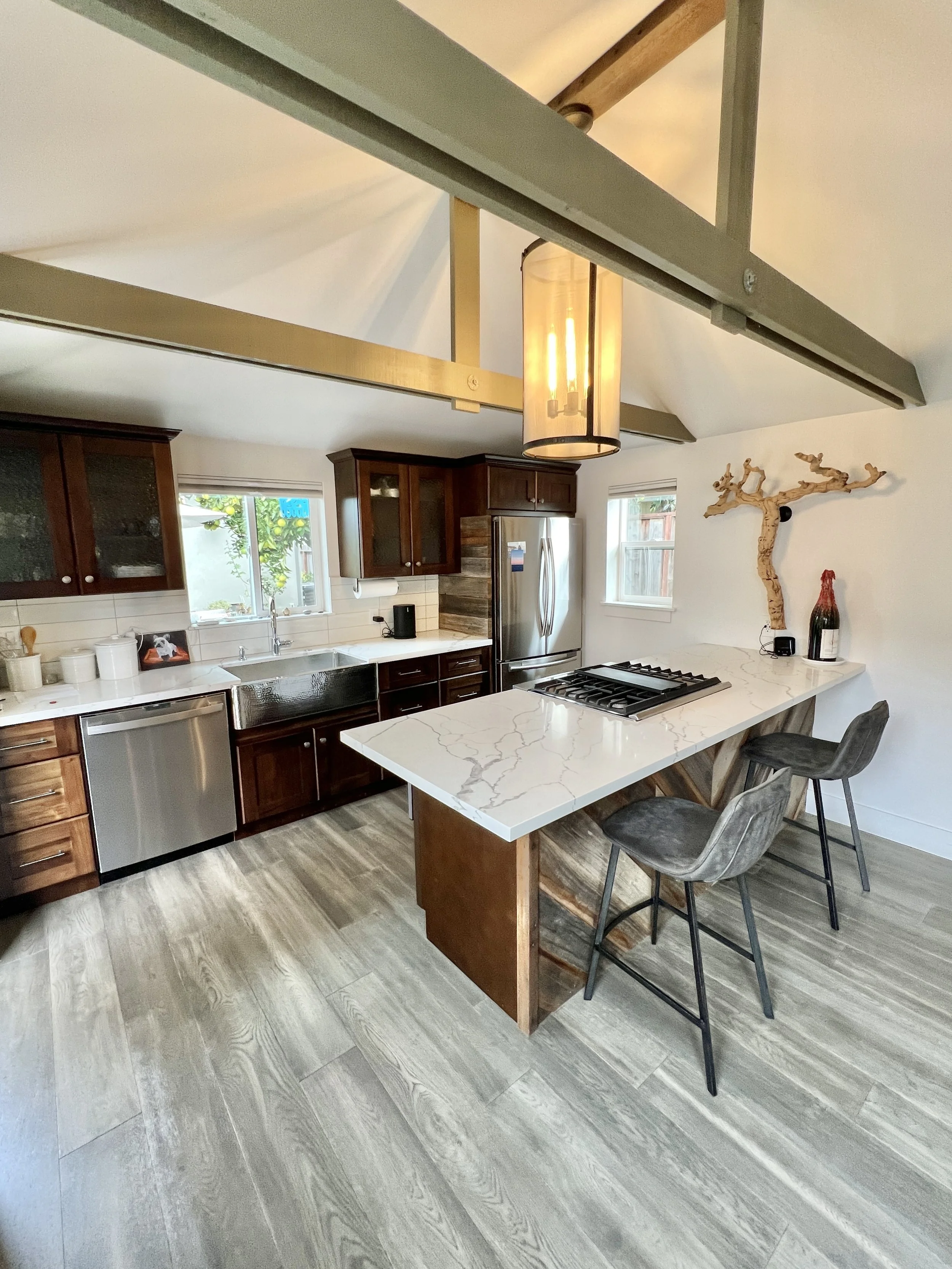 Modern kitchen with dark wood cabinets, white marble countertop, stainless steel appliances, and a wooden dining table with barstools.