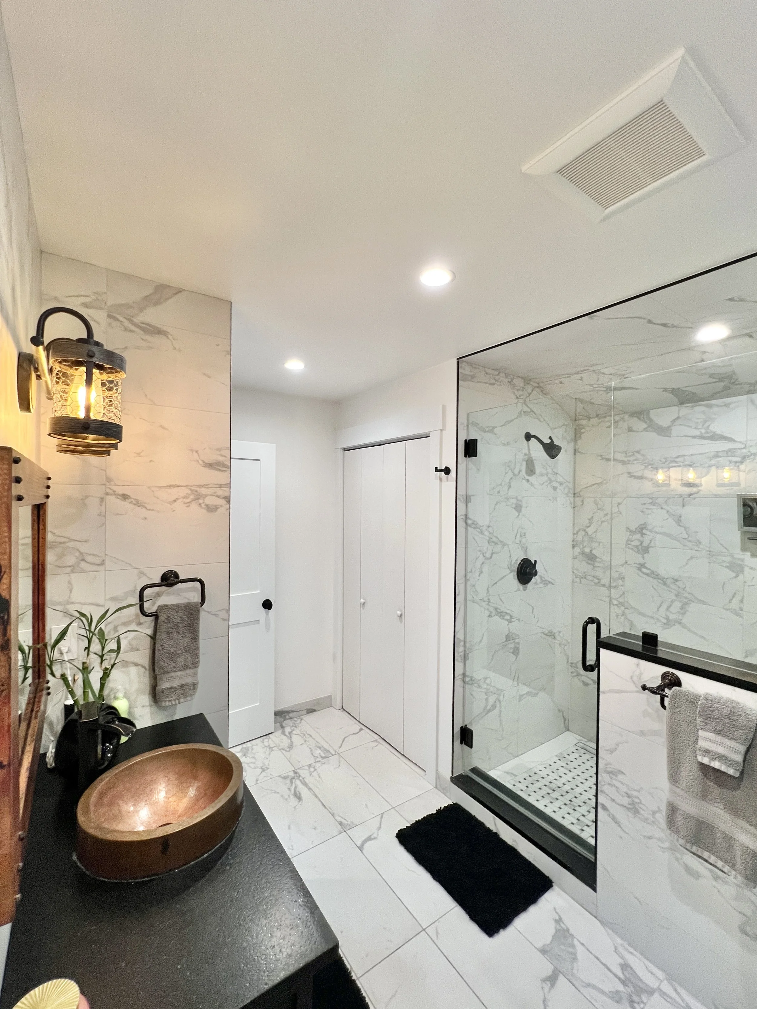 Modern bathroom with marble walls and floors, glass shower enclosure, black fixtures, white doors, and a wooden vessel sink on a black countertop.