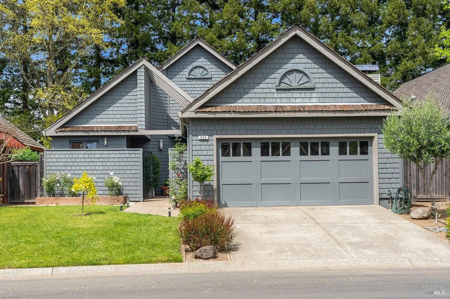 Gray house with a garage, small front yard, and trees in the background.
