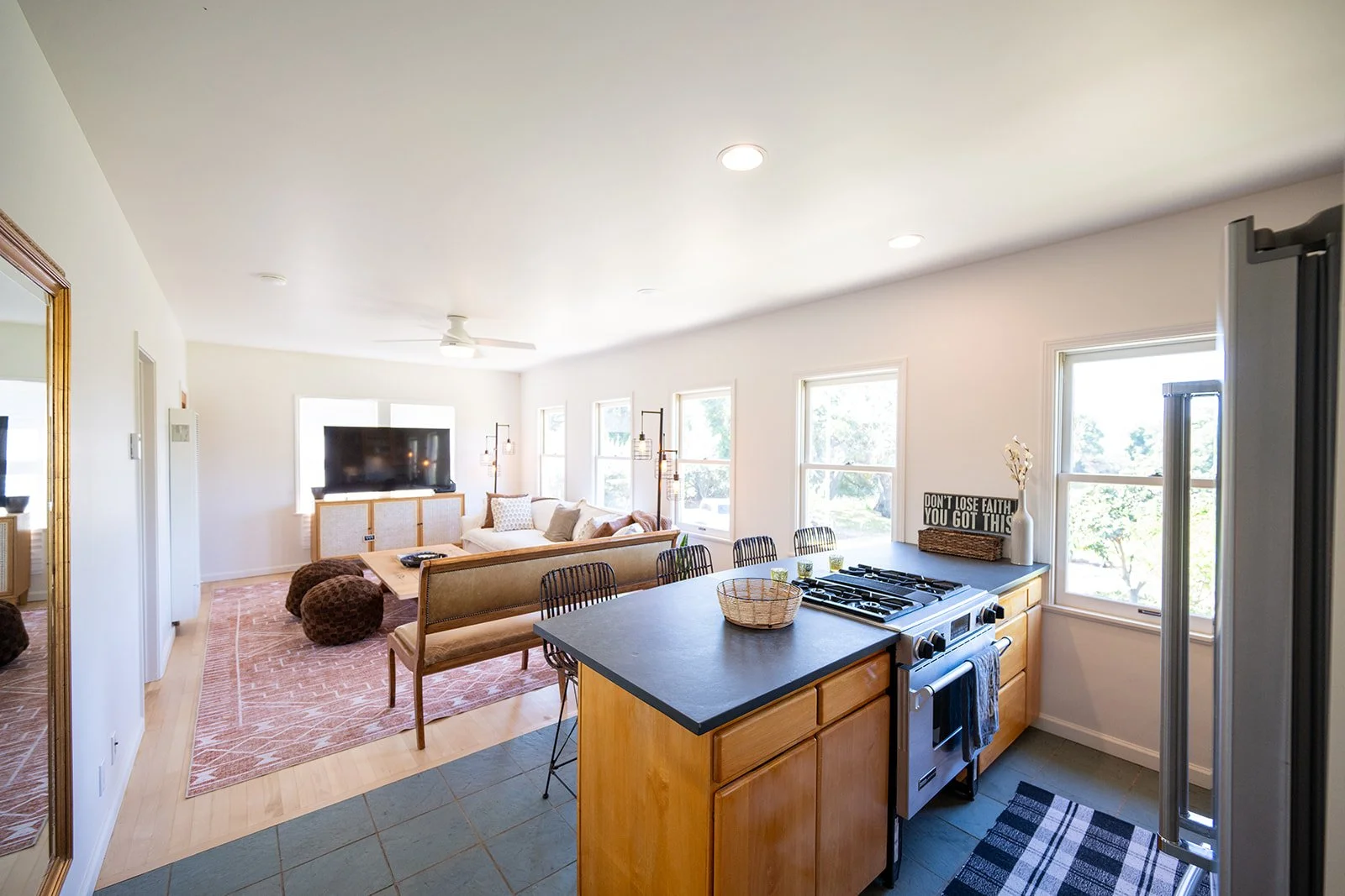 Open-concept living room and kitchen with natural light, beige furniture, and modern decor.