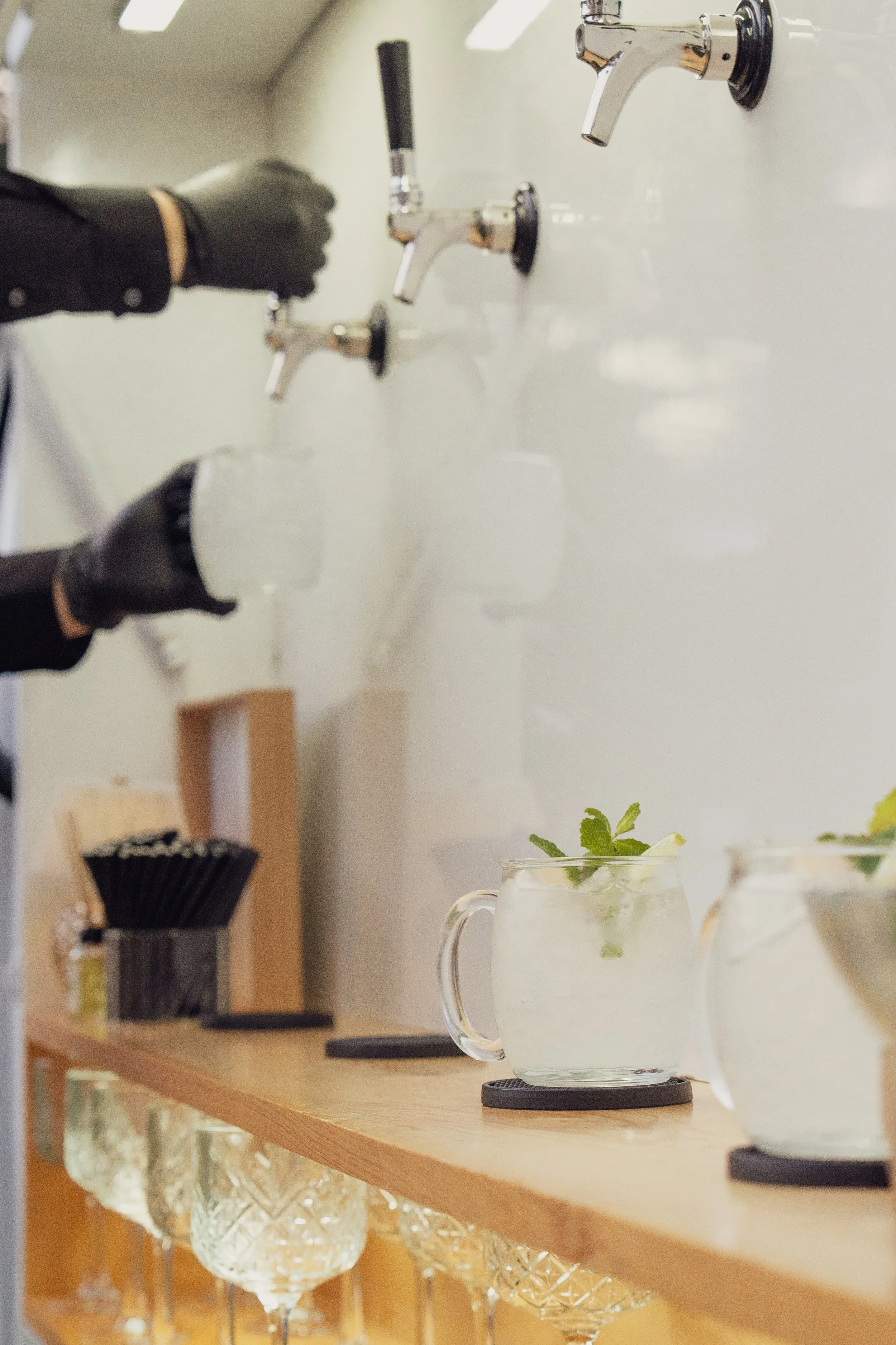 Bartender wearing black gloves preparing drinks with tap water, with glassware and mint garnish on the counter.