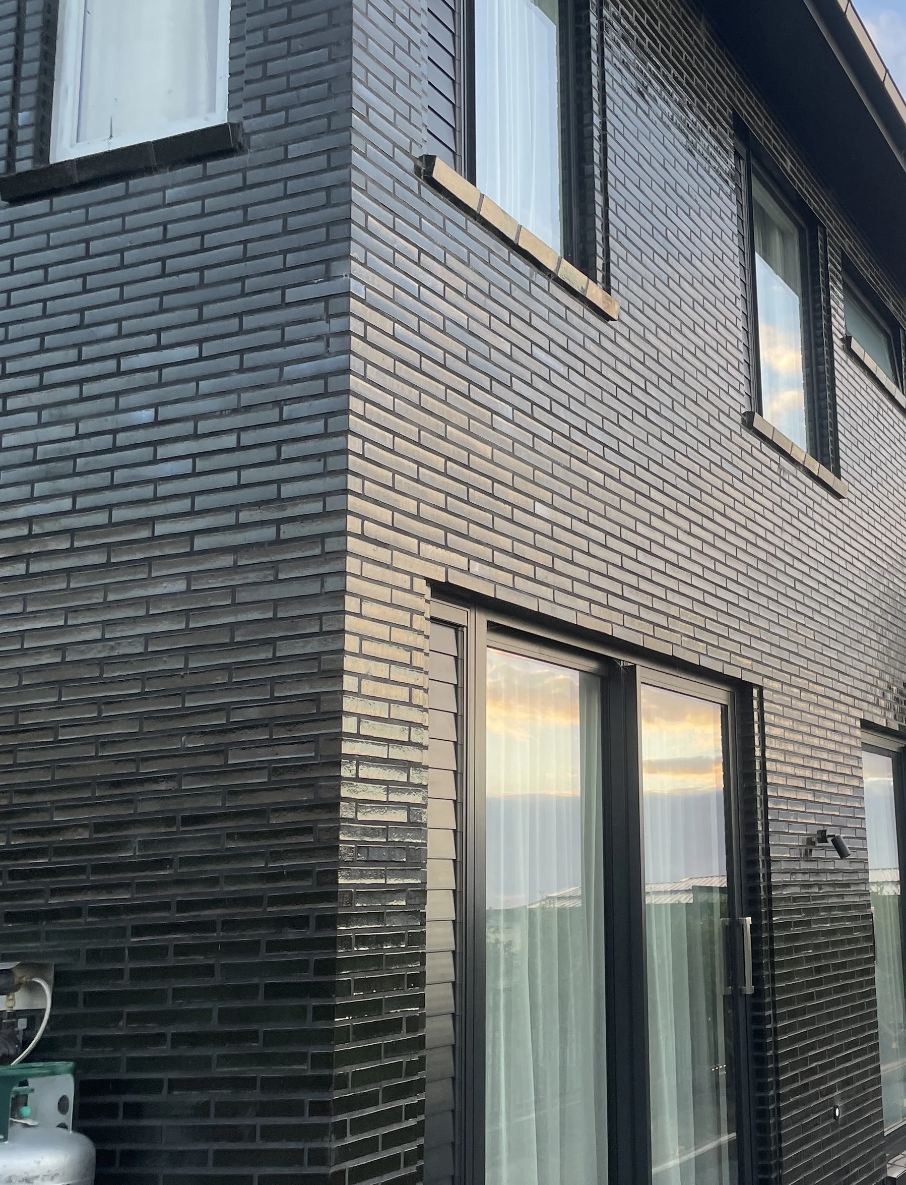 Close-up view of a modern building's black brick exterior with windows reflecting a sunset sky.