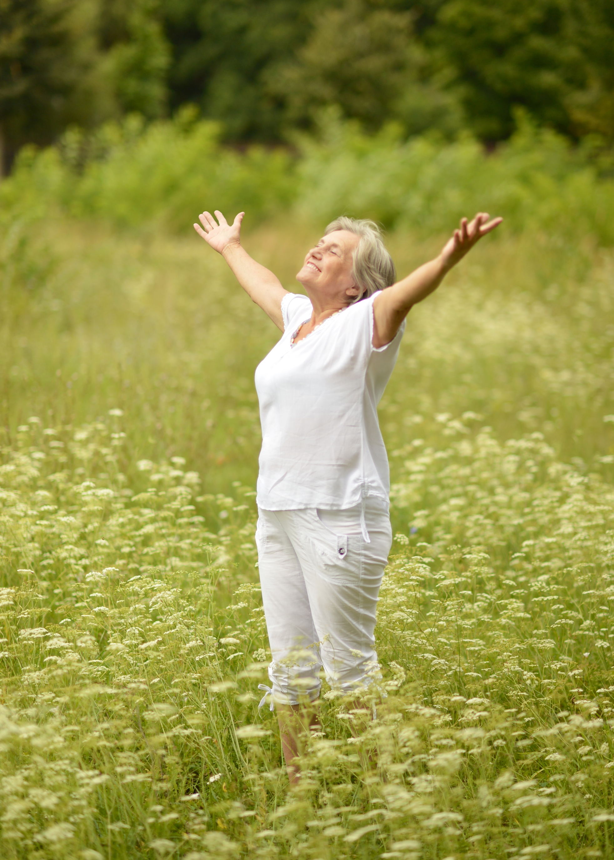 Woman smiling with arms raised outdoors, embodying renewal and personal growth inspired by Ruth Olson Coaching.