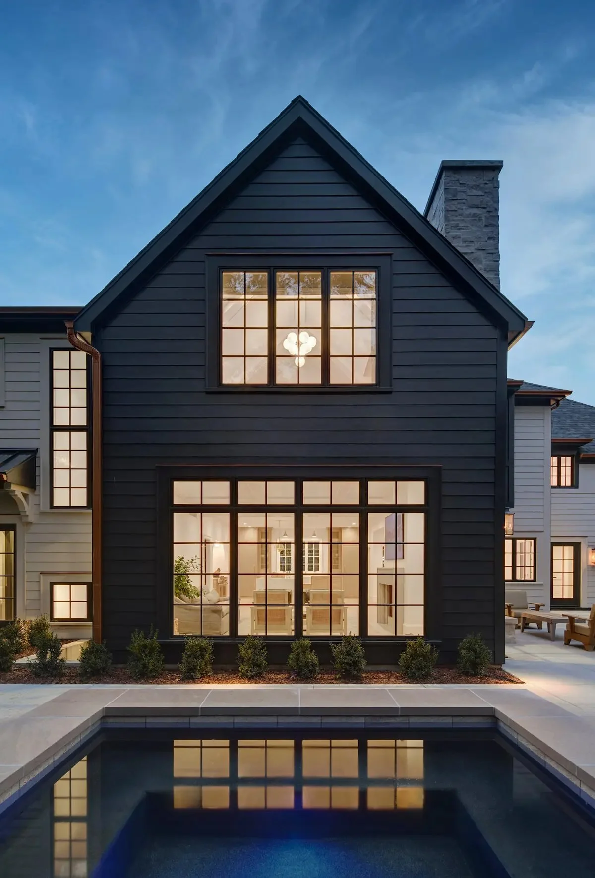 Modern two-story house with large windows, a backyard pool, and outdoor seating at dusk.