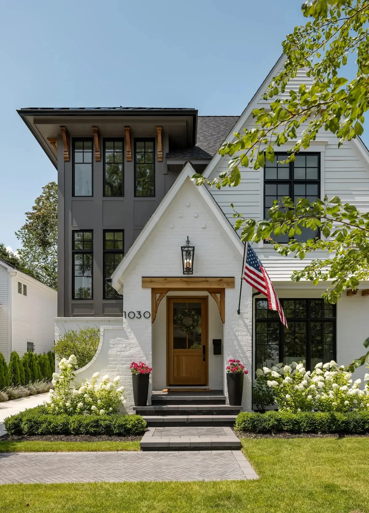 Modern white house with black window frames, wooden accents, garden, and American flag.
