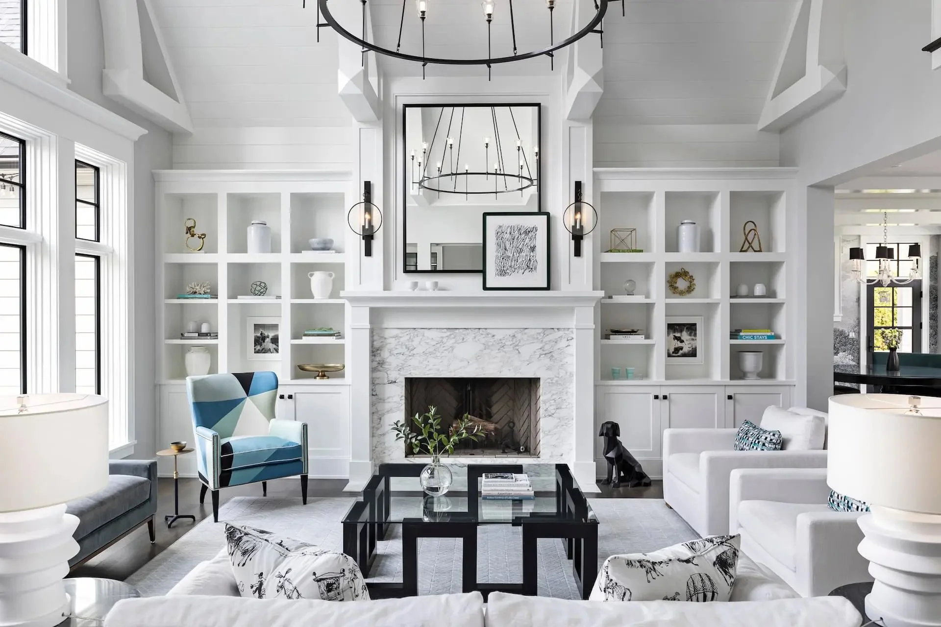 Modern living room with white walls, a marble fireplace, built-in white bookshelves, black chandelier, and black side tables.