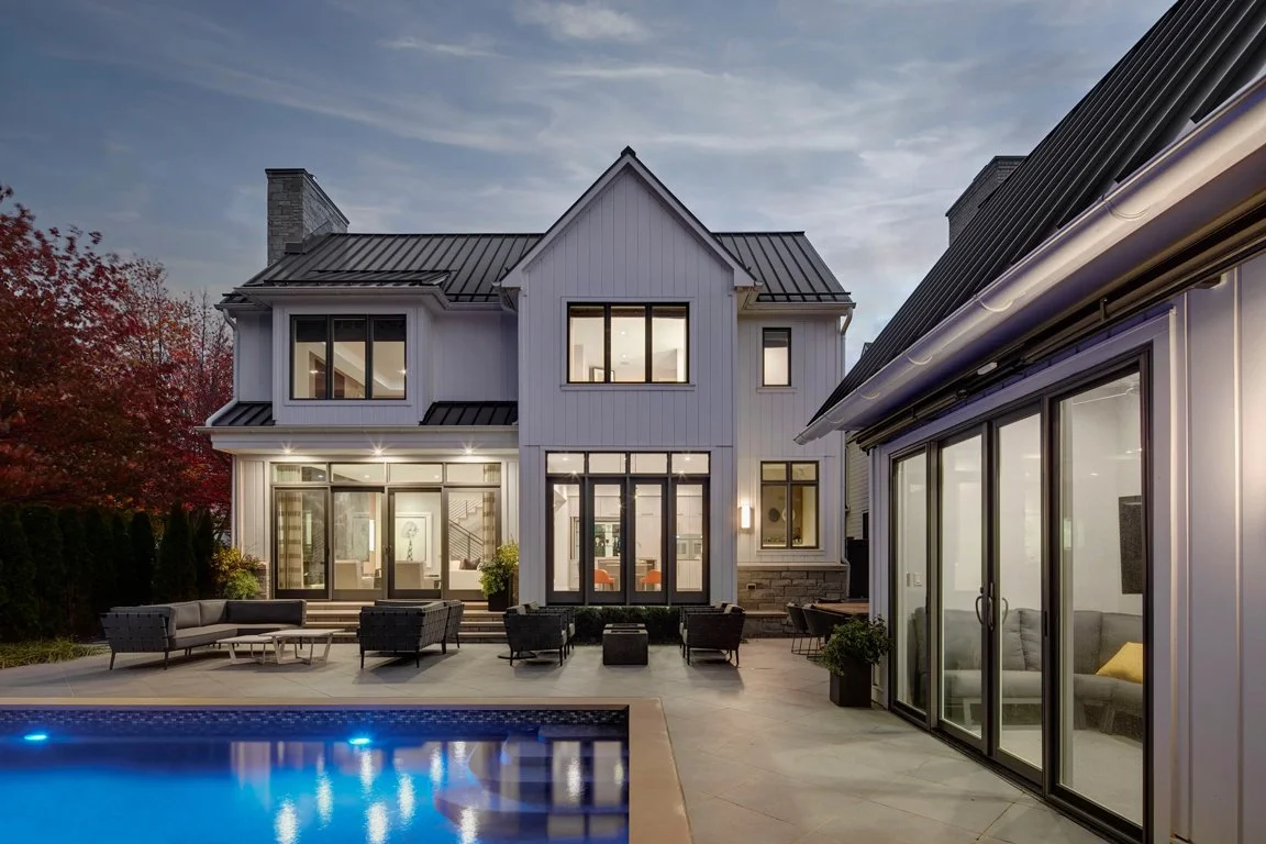 Modern two-story house with a backyard patio, outdoor seating, and a swimming pool, during dusk.