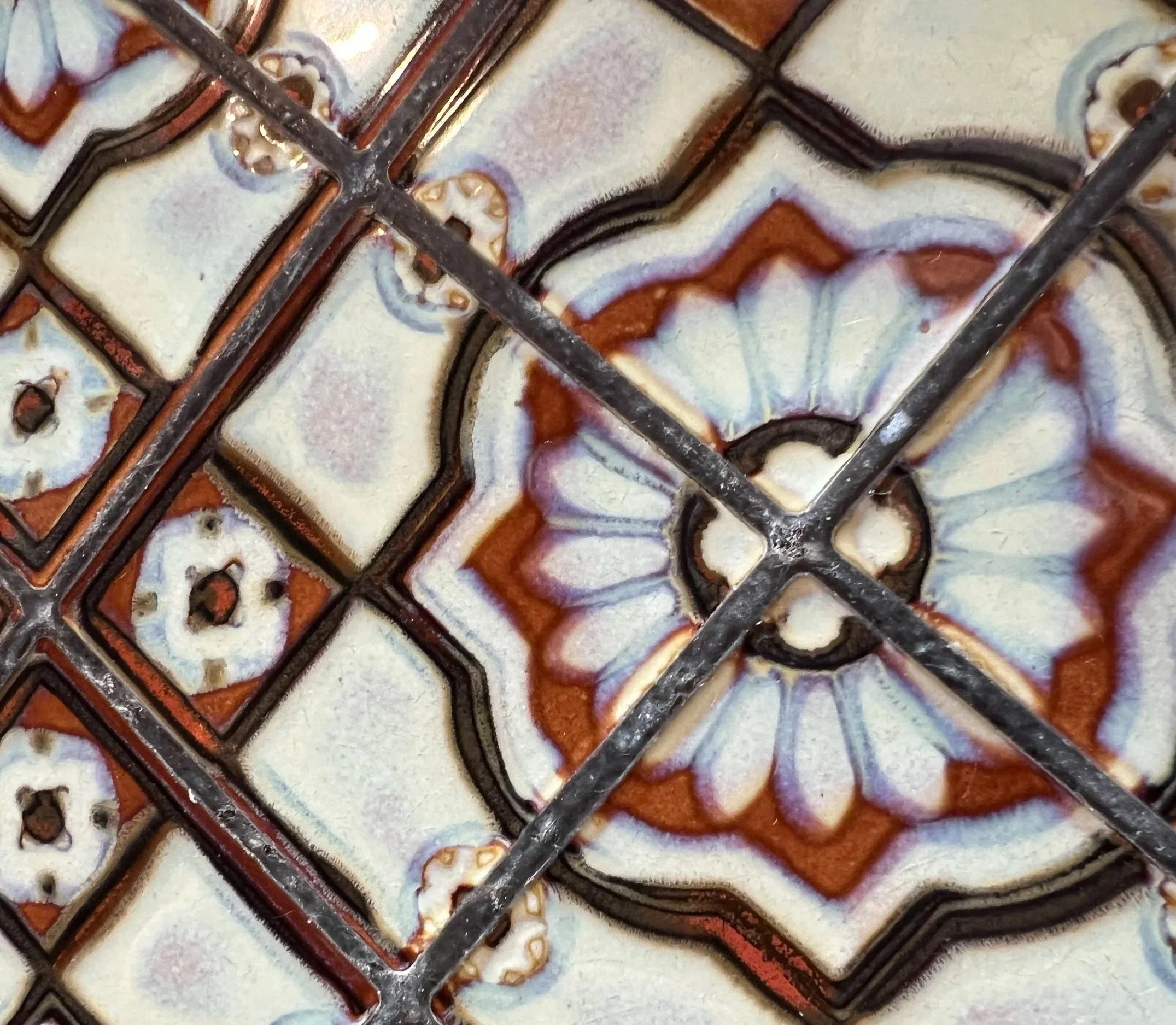 Close-up image of a decorative tile with intricate geometric and floral patterns outlined in black, with white, brown, and beige colors.